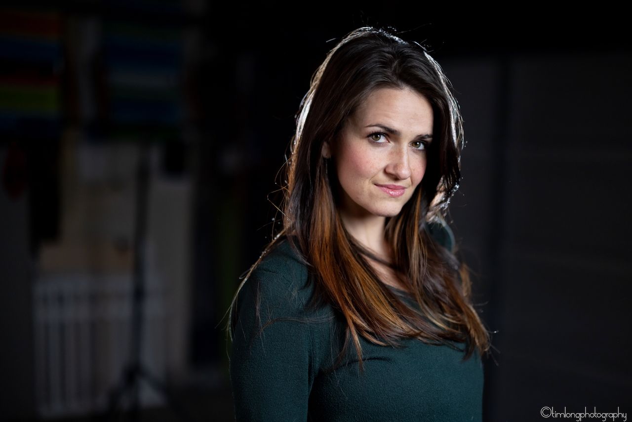 Professional headshot of a woman wearing headphones in a green sweater against dark background.