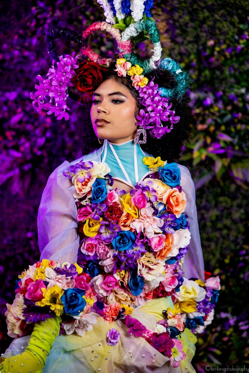 Colorful floral costume with vibrant roses and purple accents against dark background.