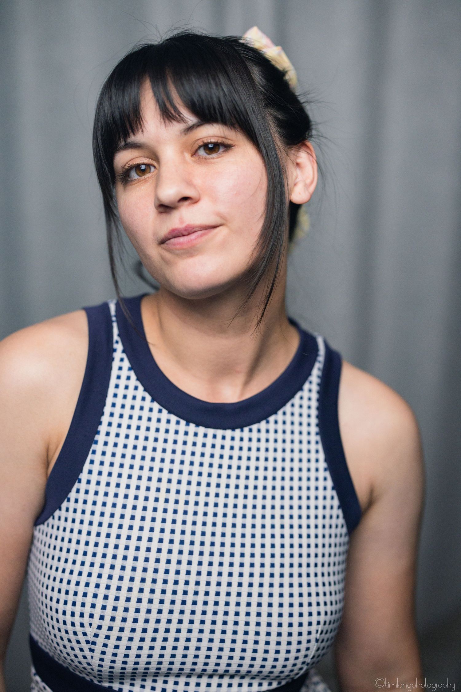 Portrait series in navy and white polka dot sleeveless top against grey background.