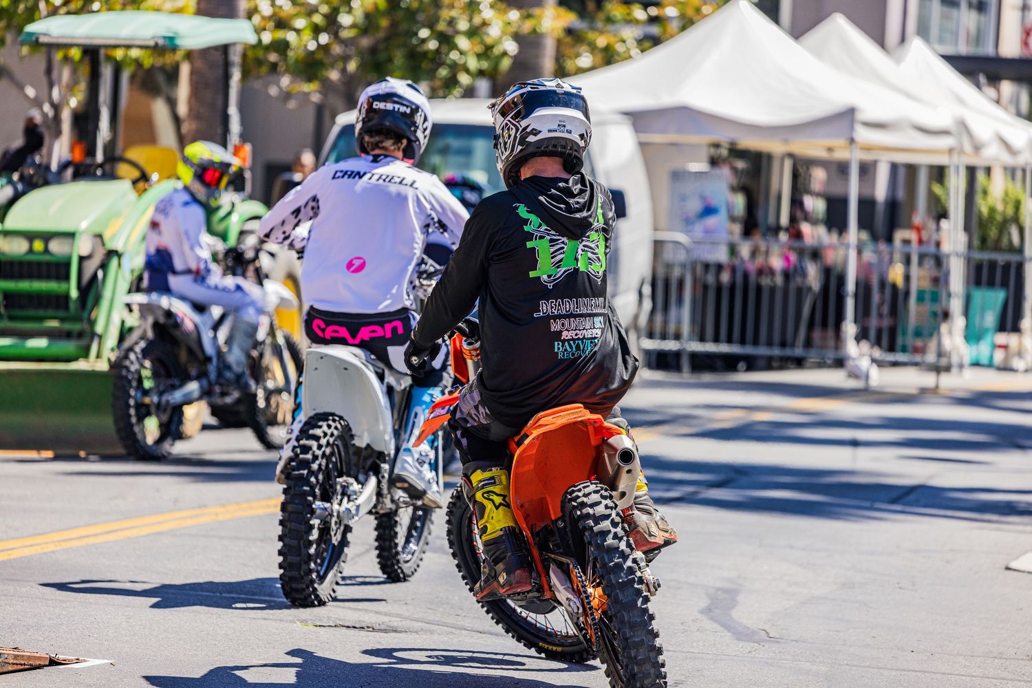 Stunt motorcyclists showcasing tricks on an urban street during a daytime event.