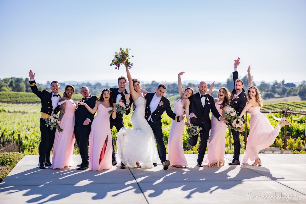 Wedding party poses together in vineyard setting wearing pink and black formal attire.