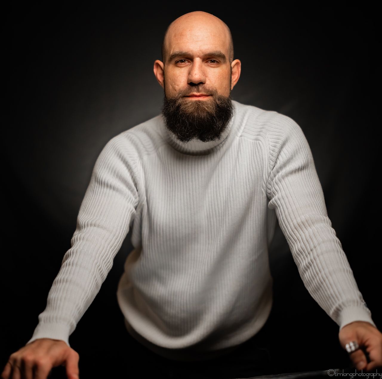 Studio portrait of a bearded man in a light gray sweater against dark background.