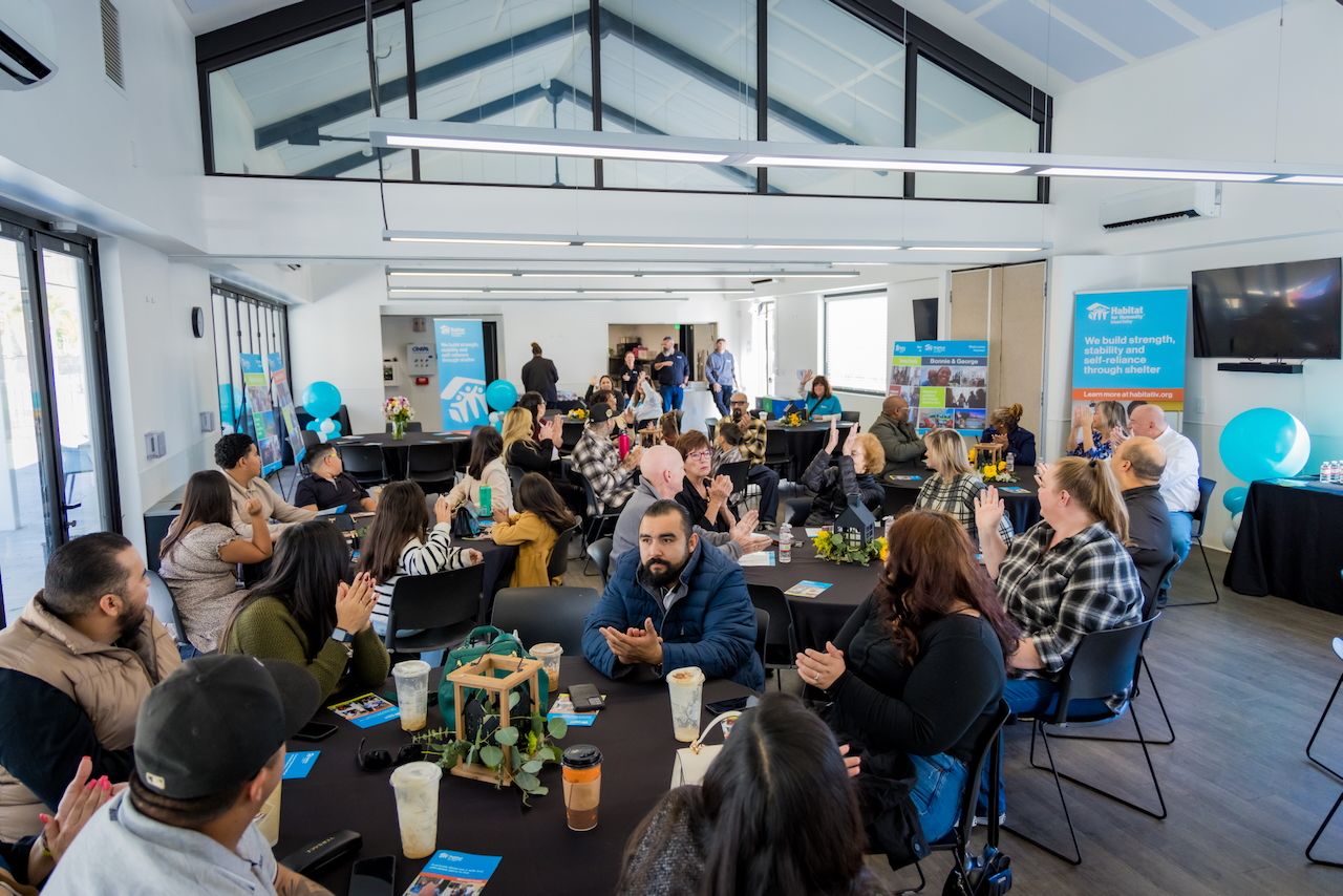 Crowded indoor event space with people seated at tables under vaulted ceiling.