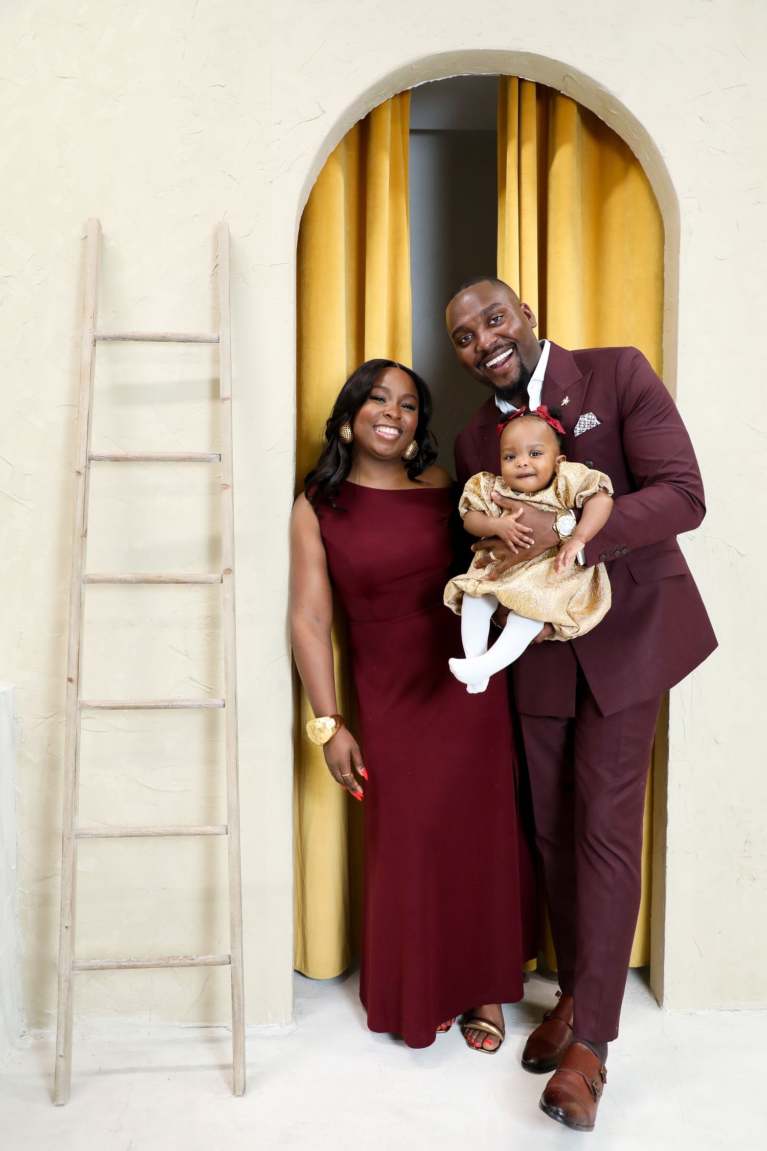 Burgundy and gold themed holiday family portrait session with elegant archways and rustic ladders.