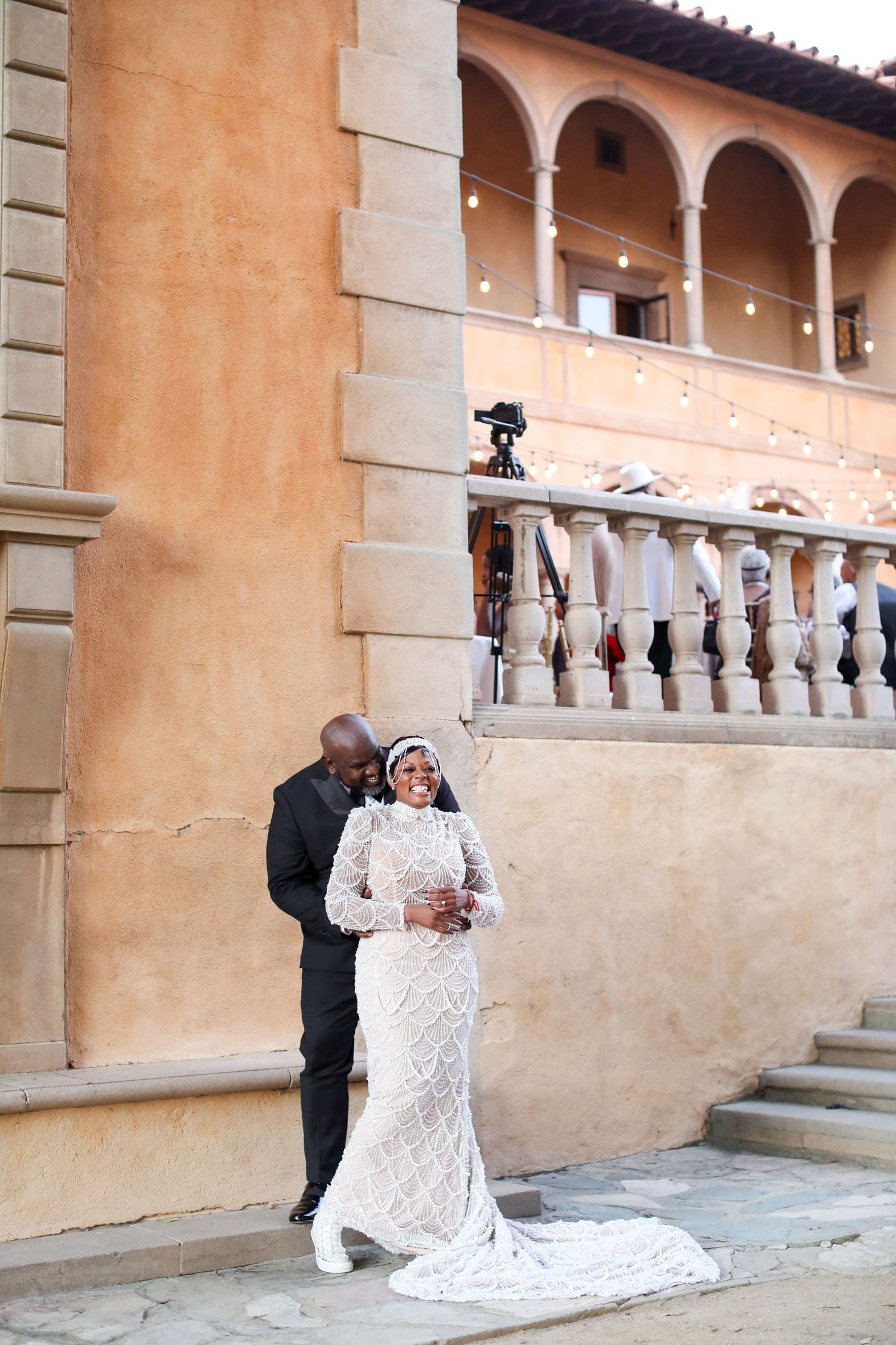Wedding couple poses against Mediterranean-style architecture with arched columns.