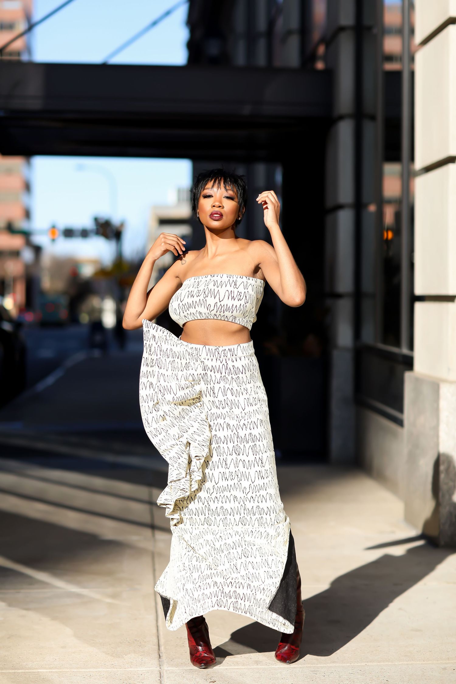 Dynamic fashion pose on sidewalk featuring white text-printed dress and red shoes.