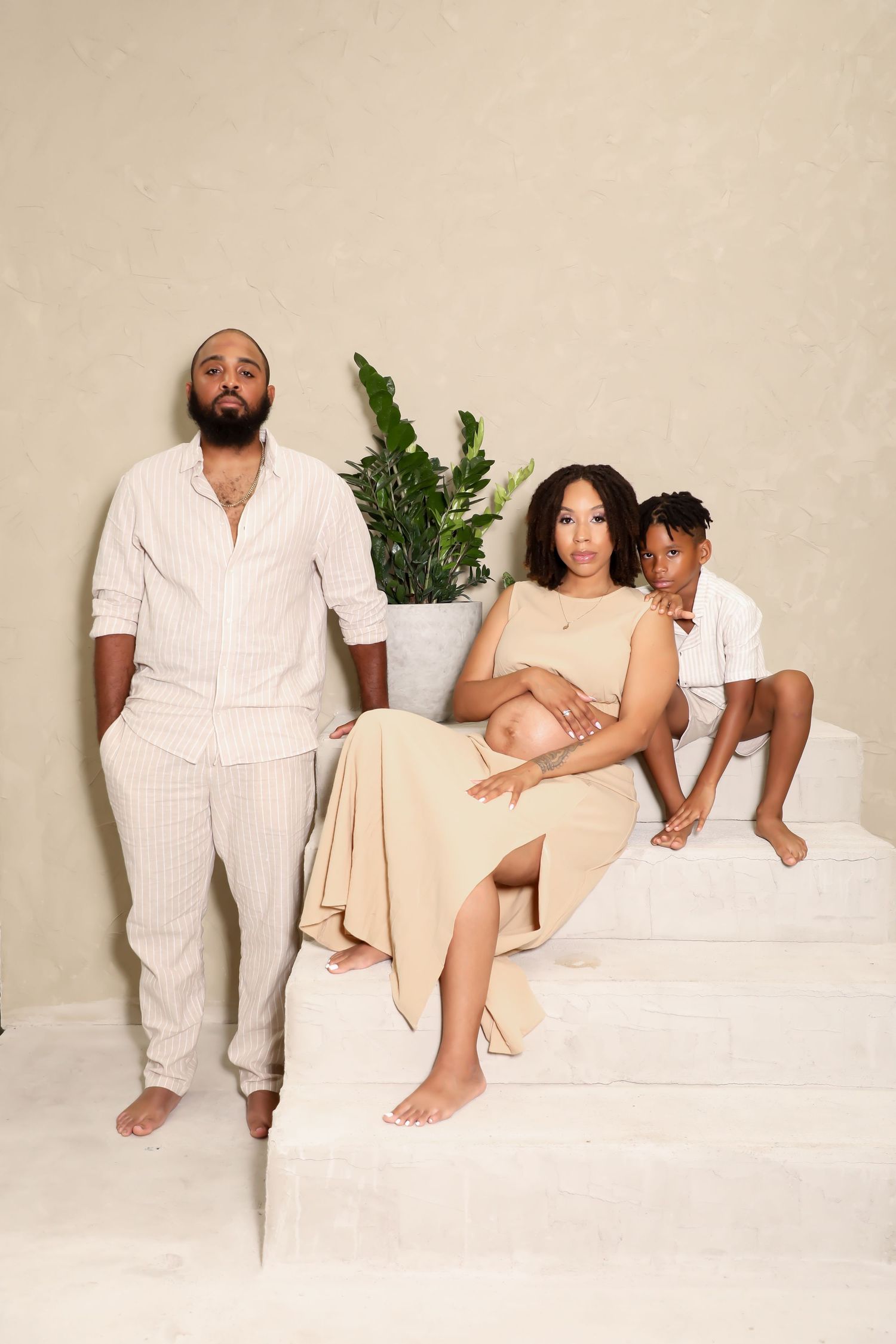 Family photo series in cream and white outfits against neutral studio backdrop with plants.