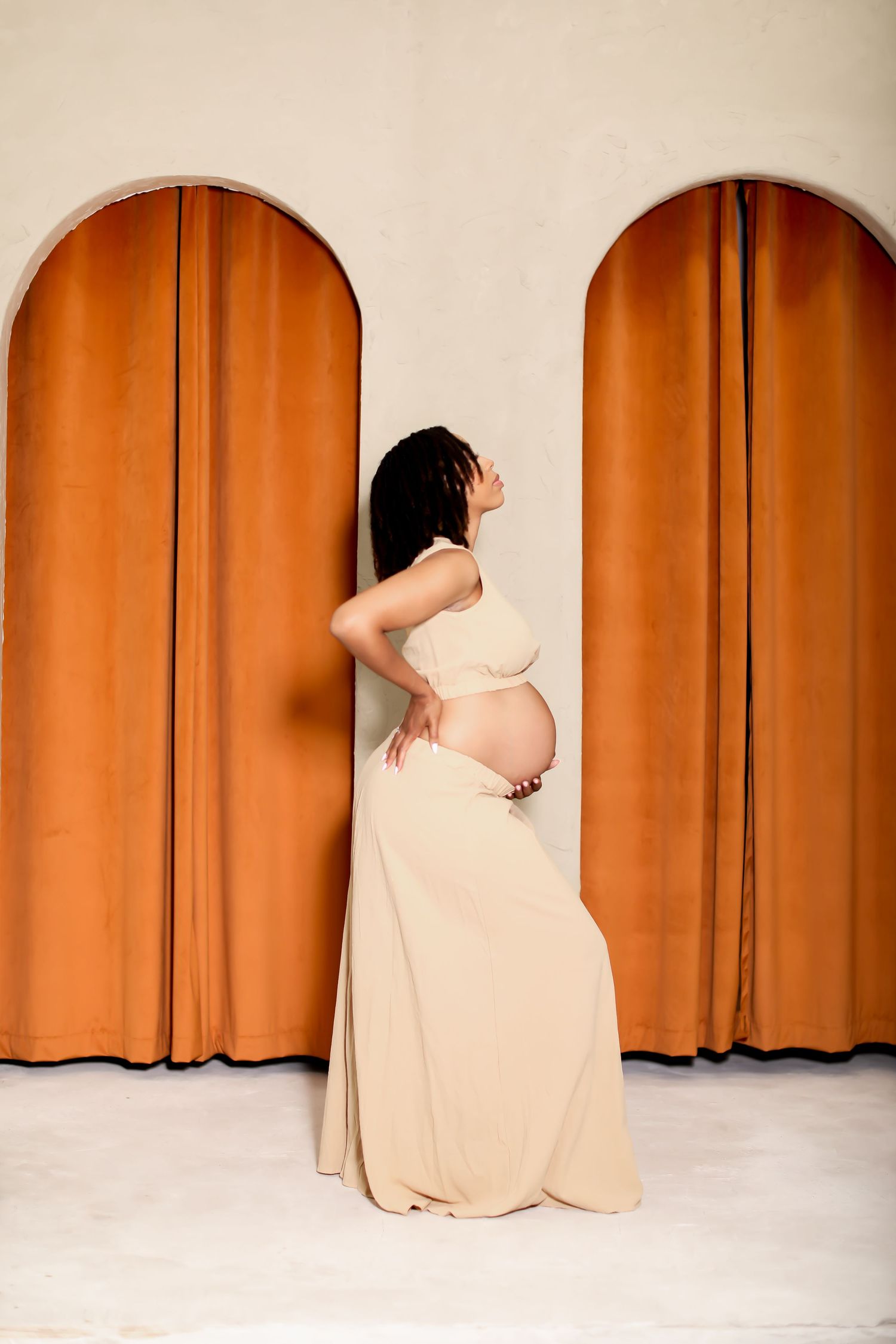 Artistic maternity poses against terracotta arched backdrop in minimalist setting.