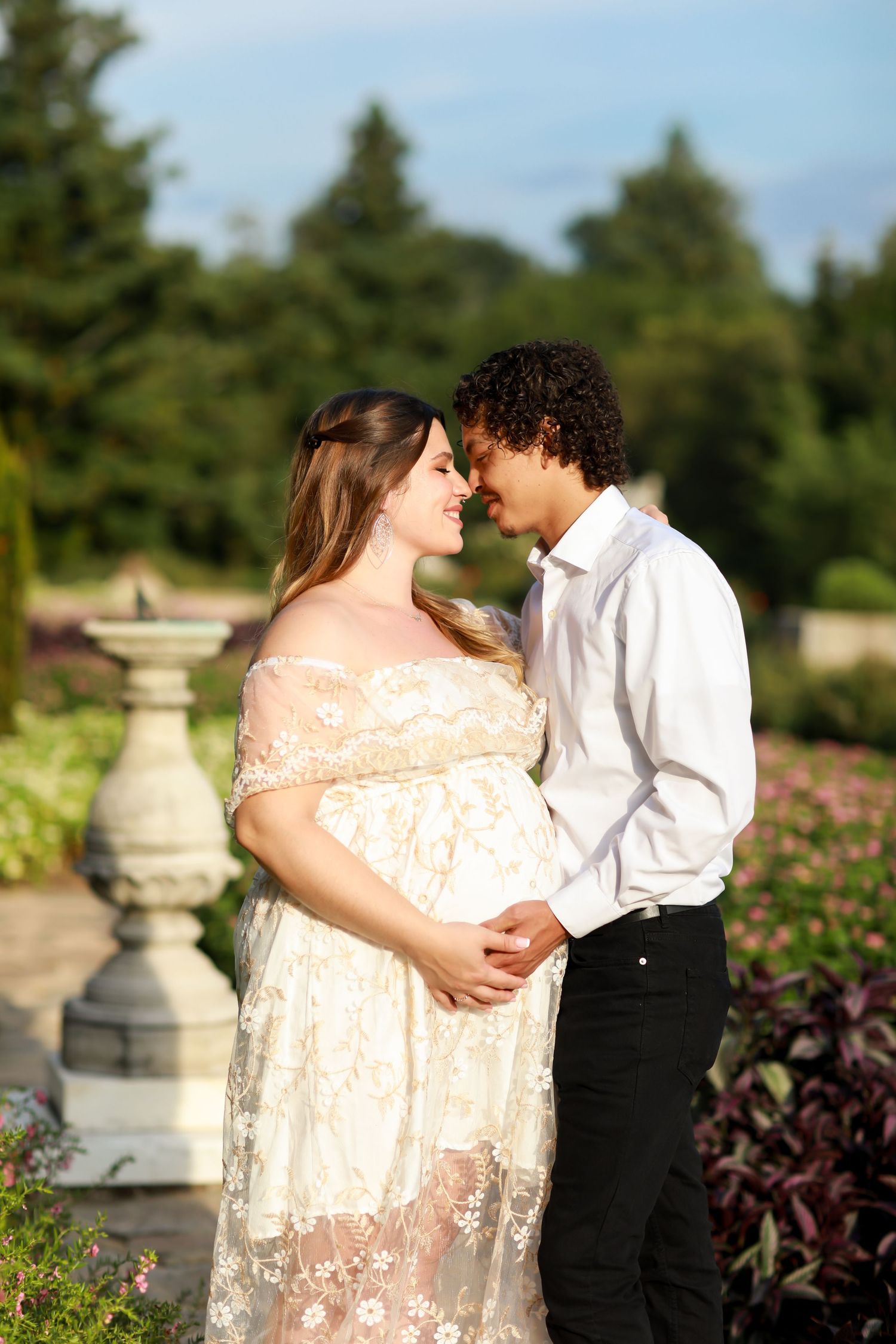 Couple embracing in garden setting with stone pillars and flowering plants.