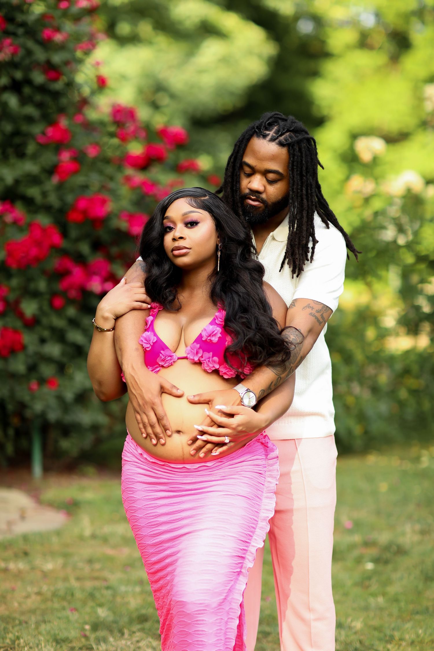 Romantic outdoor maternity photoshoot among blooming rose bushes in a garden.
