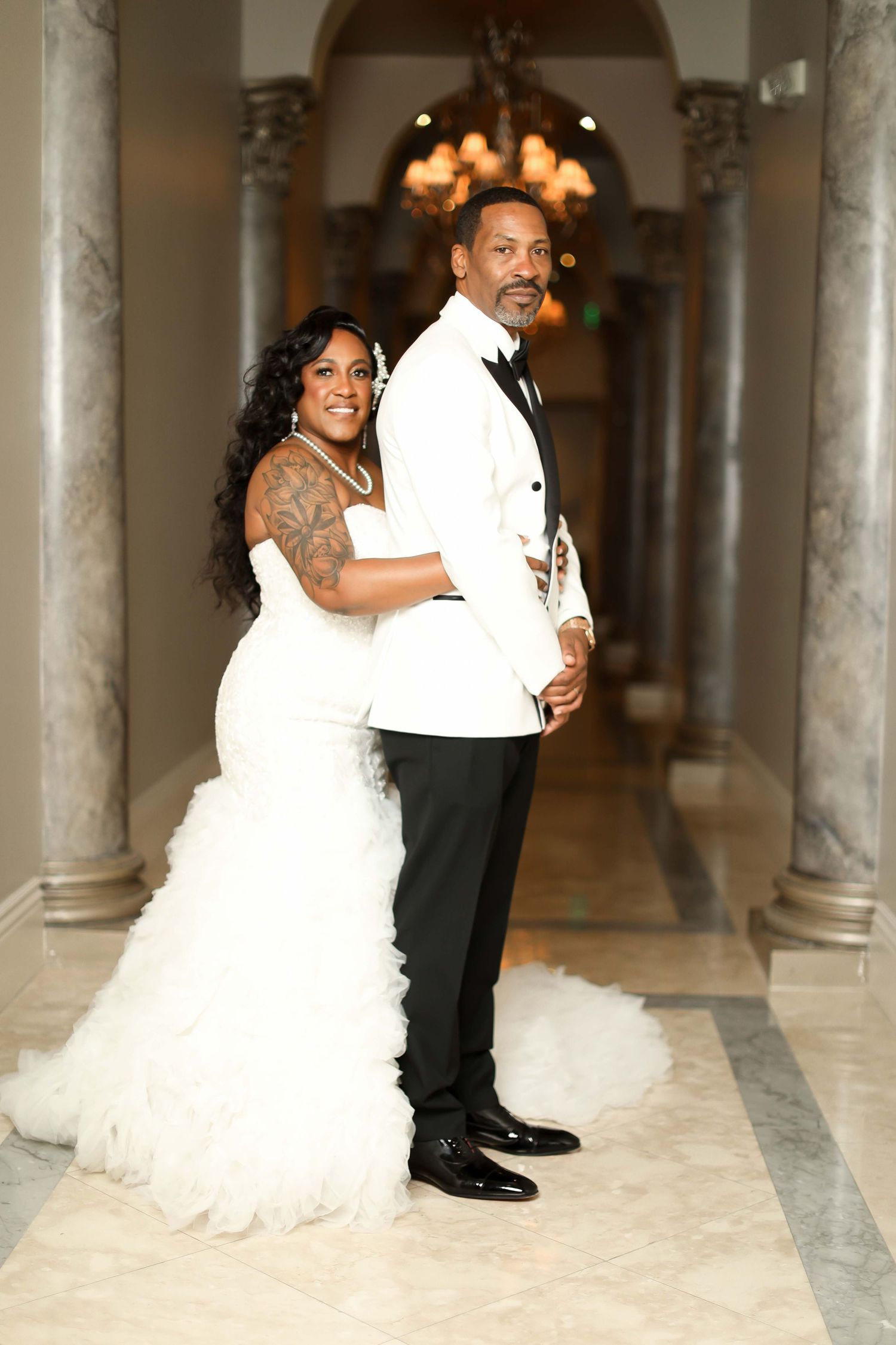 Elegant bridal couple poses in ornate hallway with marble columns.