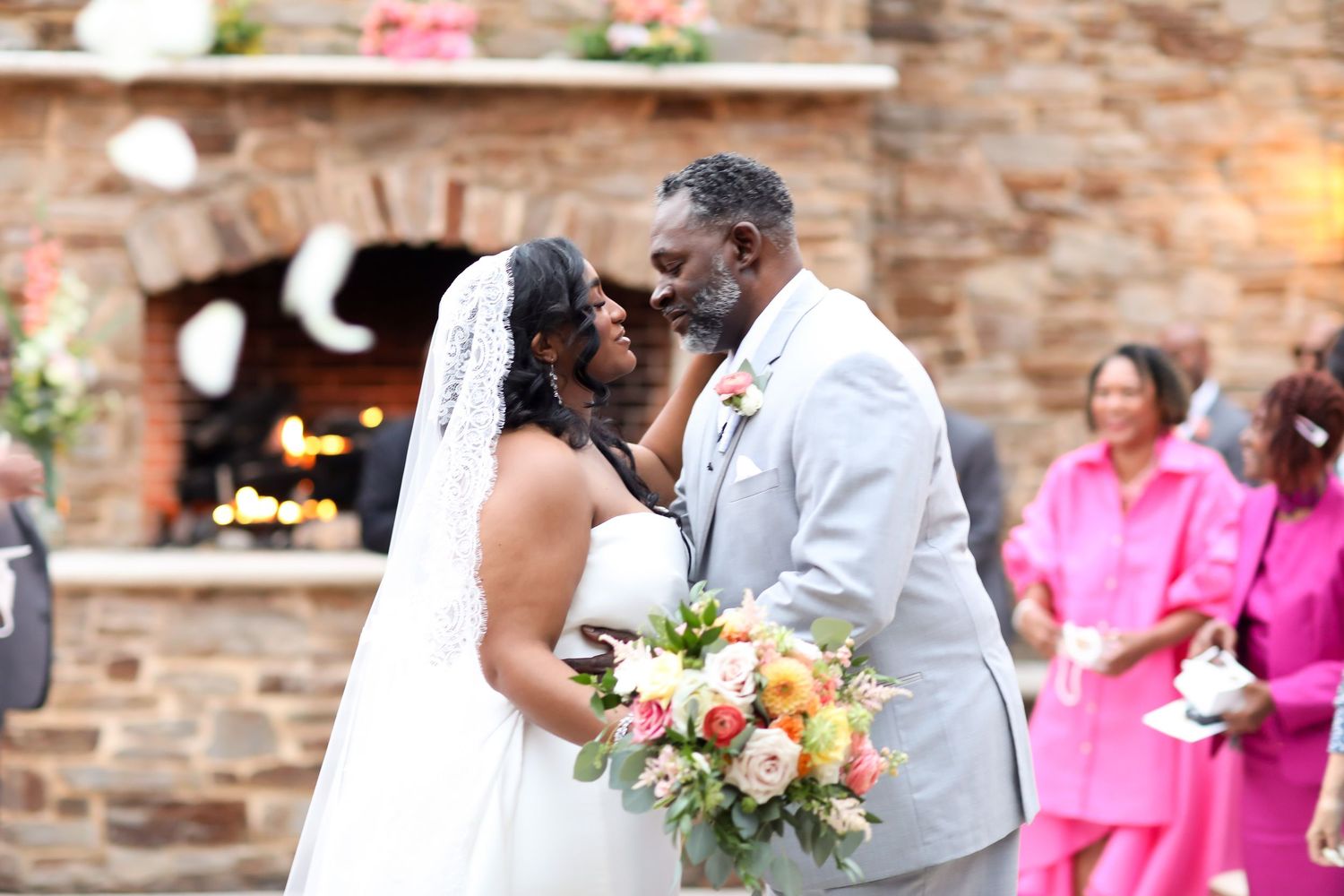 Wedding celebration with pink-dressed attendants against a rustic stone wall backdrop.