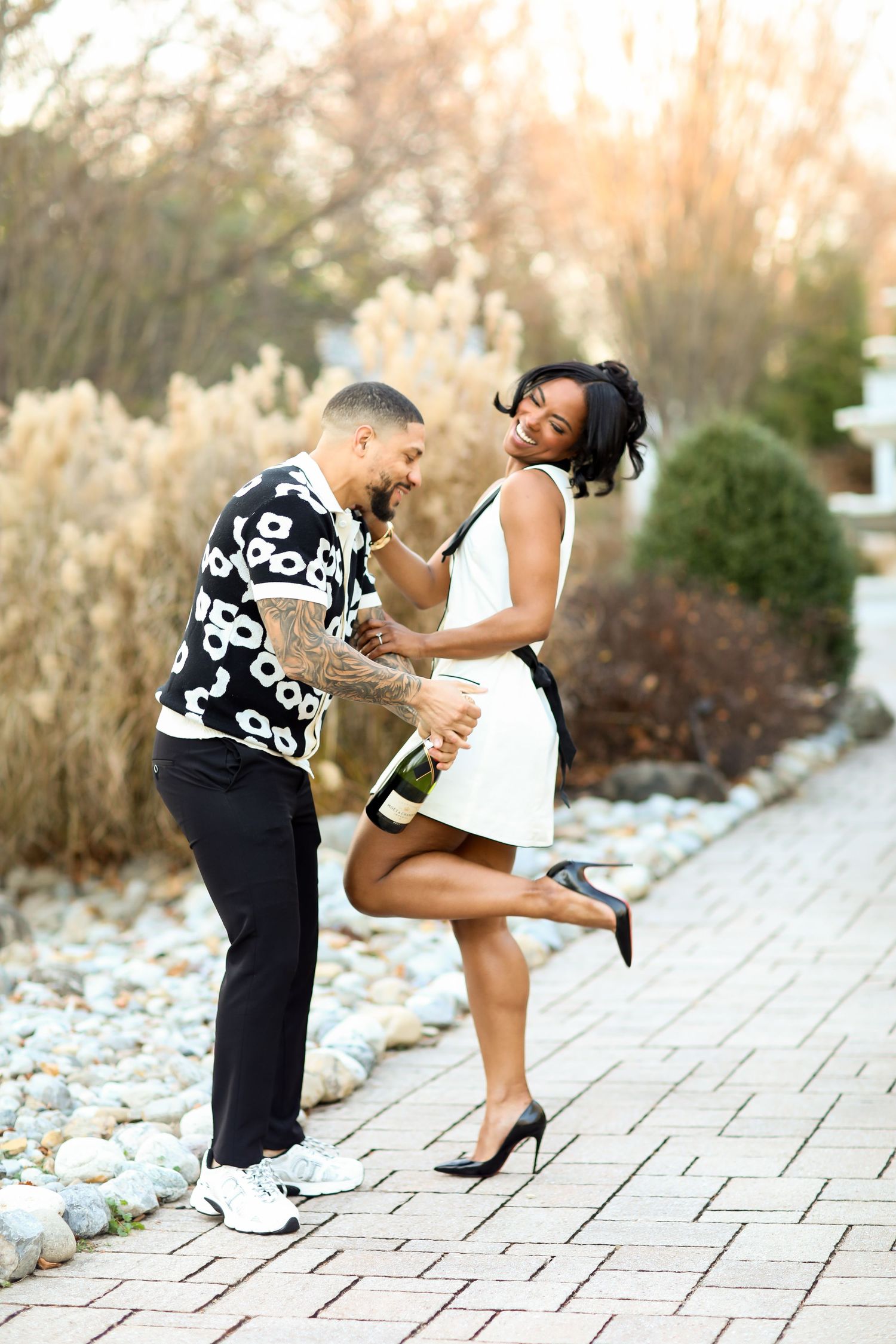 Couple playfully poses with champagne on stone pathway at sunset.