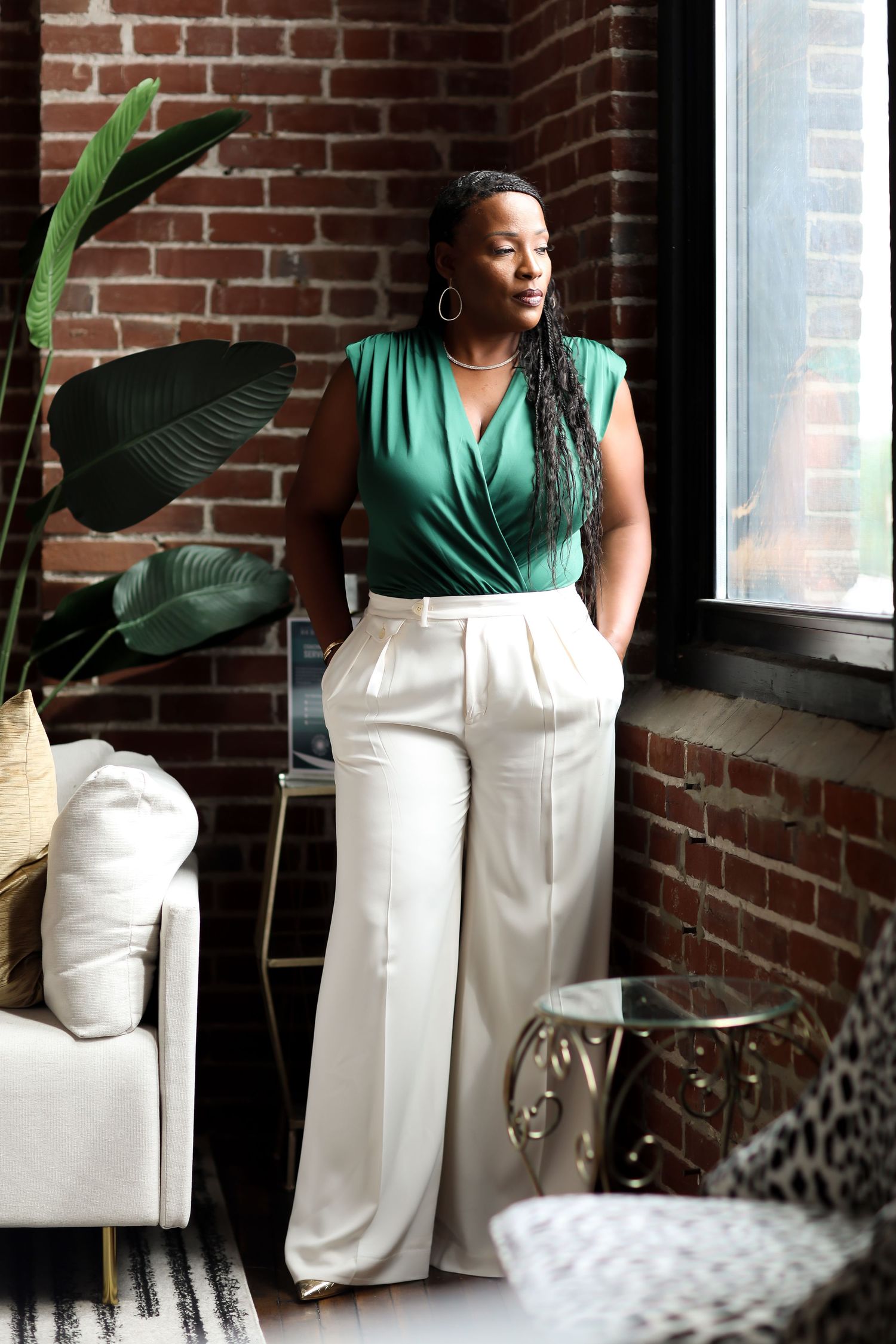 A series of five photos showing someone in a green top and white pants posing against a brick wall with indoor plants.