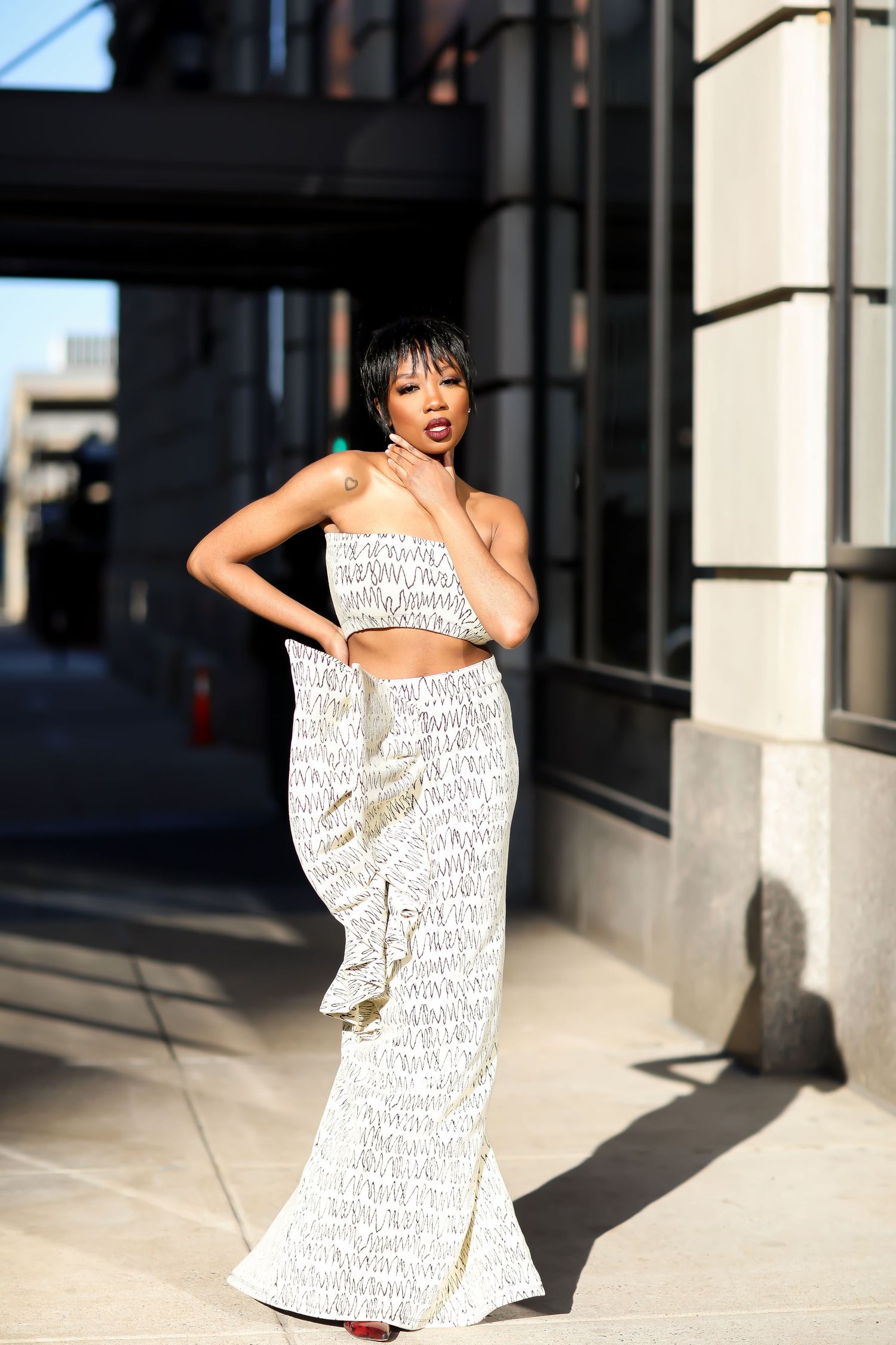 Figure in white text-printed dress poses dramatically against urban building backdrop.