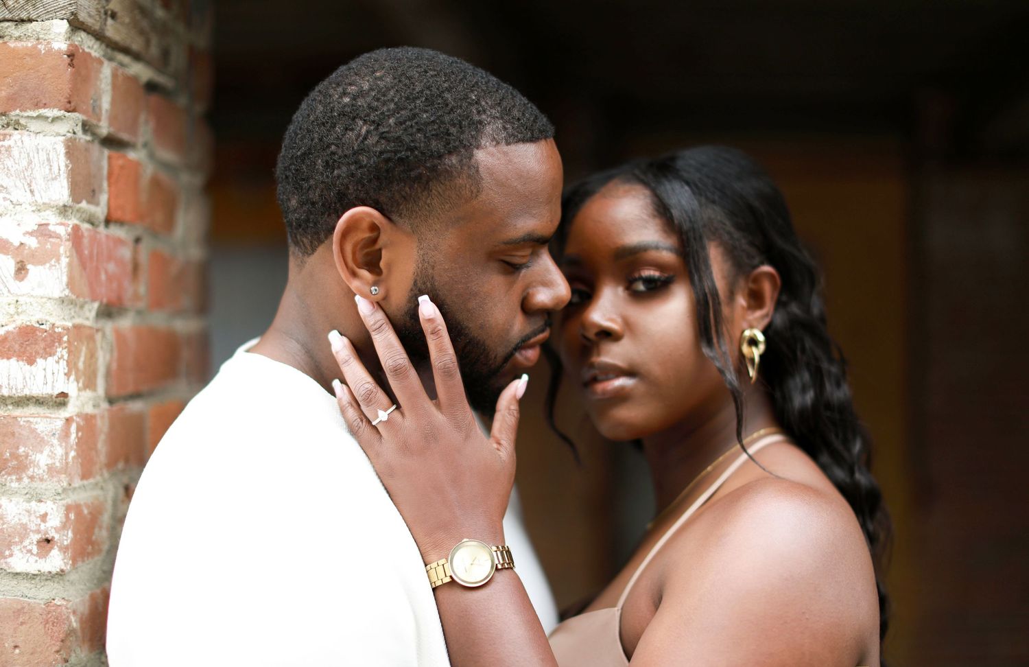 Romantic couple embracing in front of rustic brick wall during engagement photo shoot.