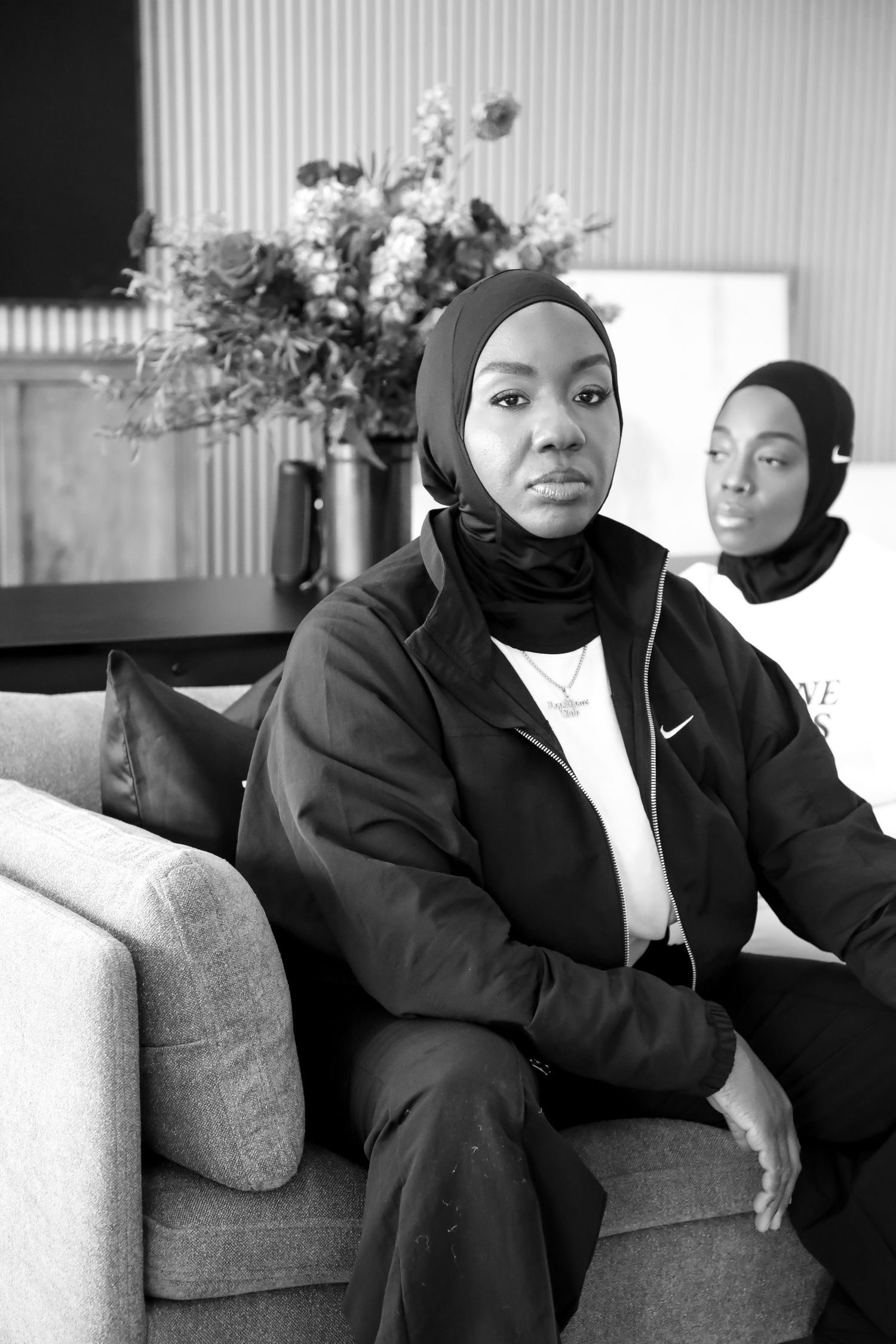 Two people sitting on a gray couch in dark clothing in a minimalist contemporary setting shown in multiple photos.