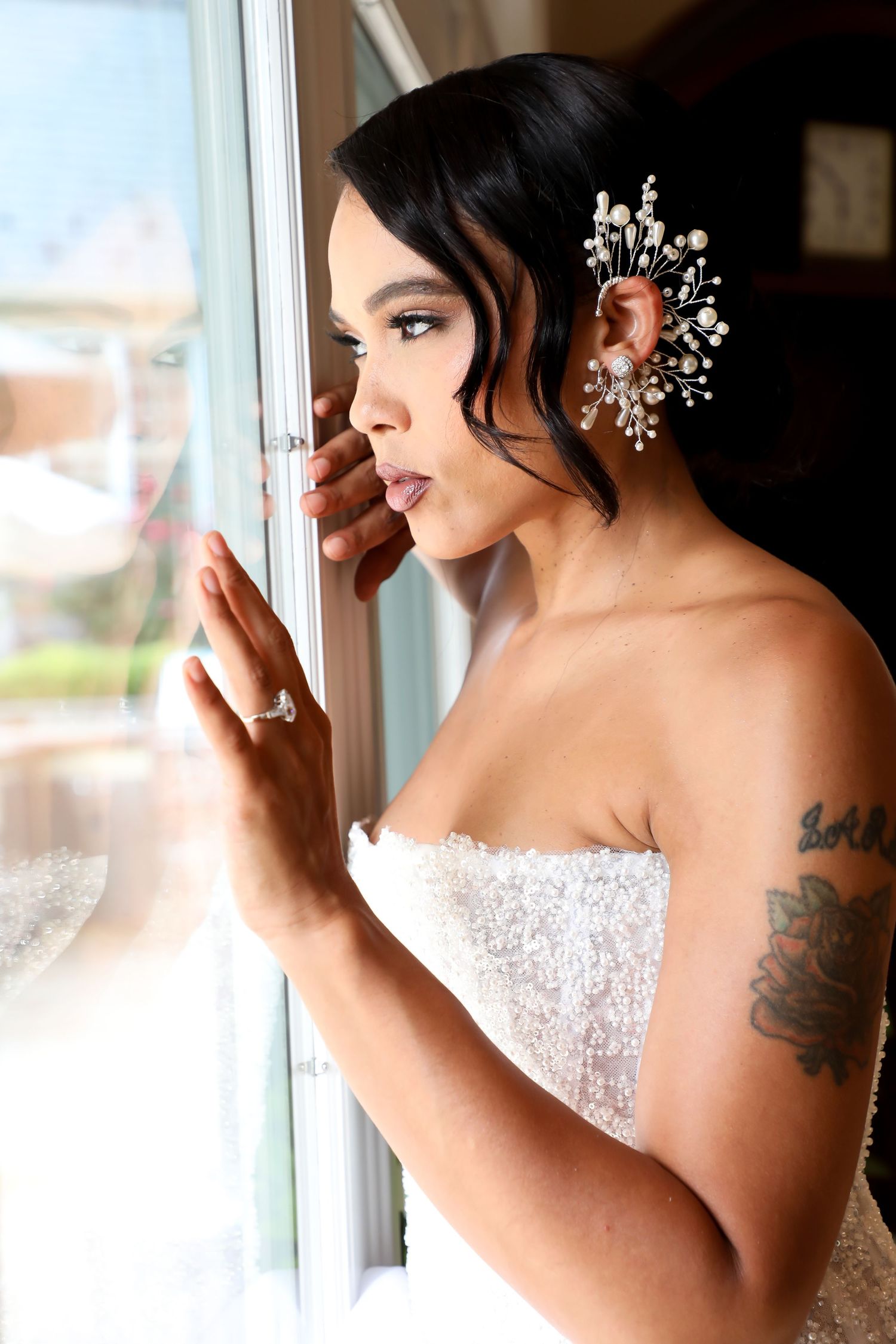 Bride wearing a white strapless dress and delicate hair accessories getting ready near a window.