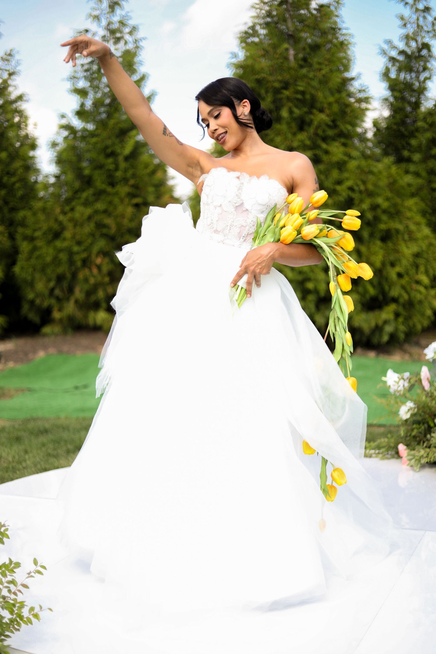 A bride twirls in her white wedding gown while holding yellow tulips outdoors.
