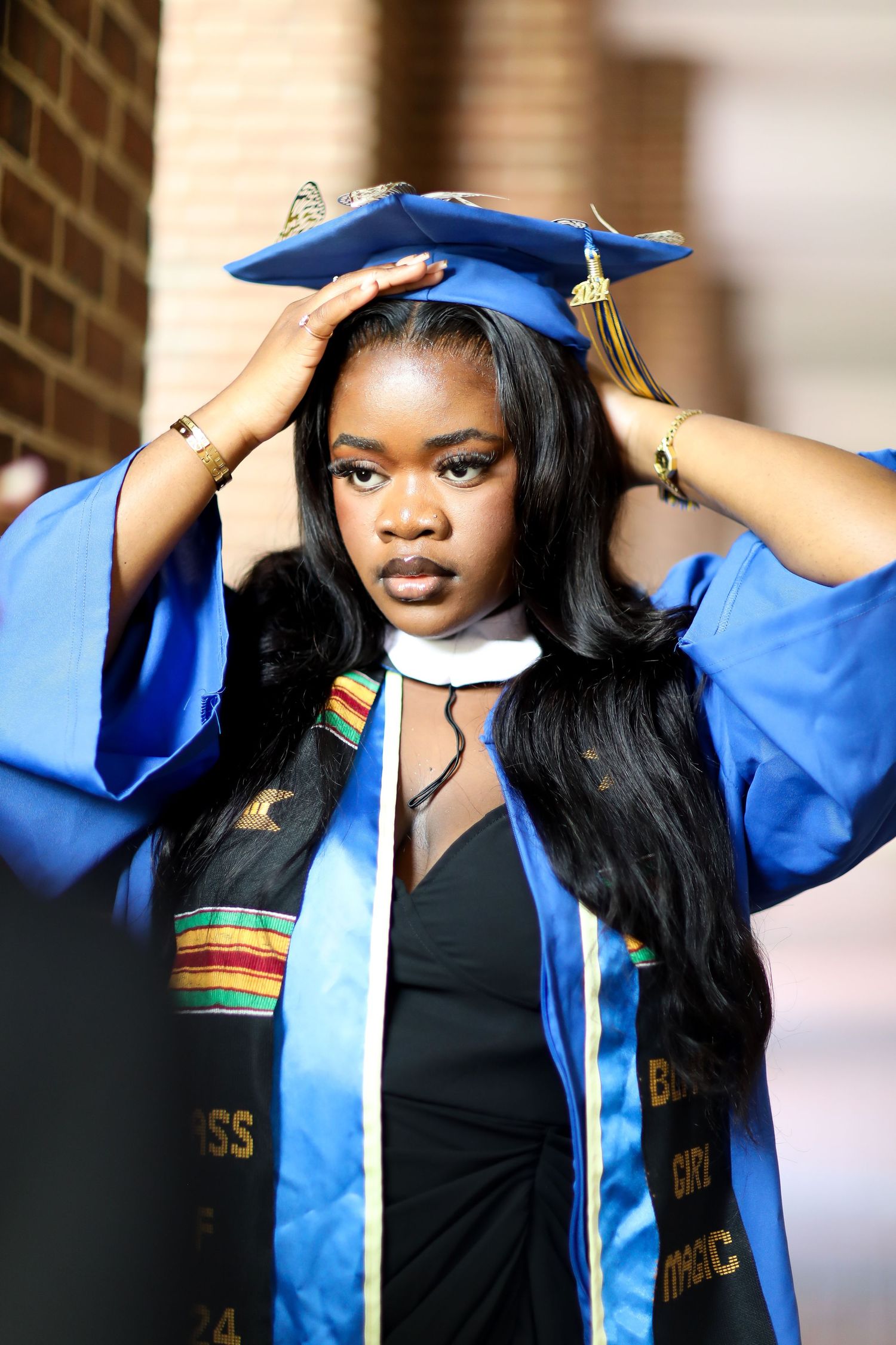 A graduation photoshoot series showing a blue cap and gown with black and gold accessories against a brick wall.