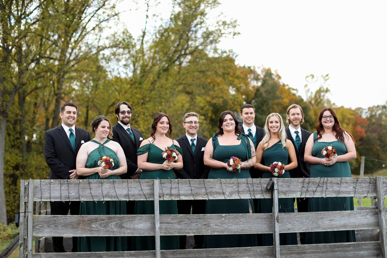 Wedding party poses together on a wooden deck or bridge outdoors.