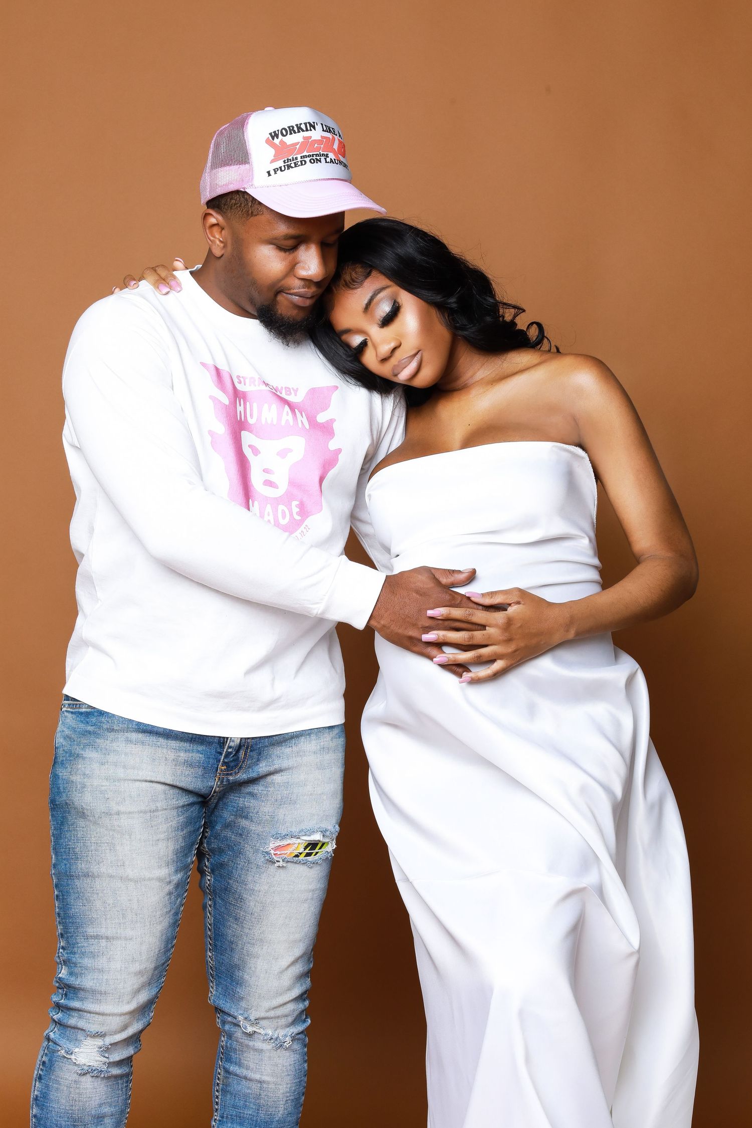 Maternity photo series with couple in white and denim against warm brown backdrop.