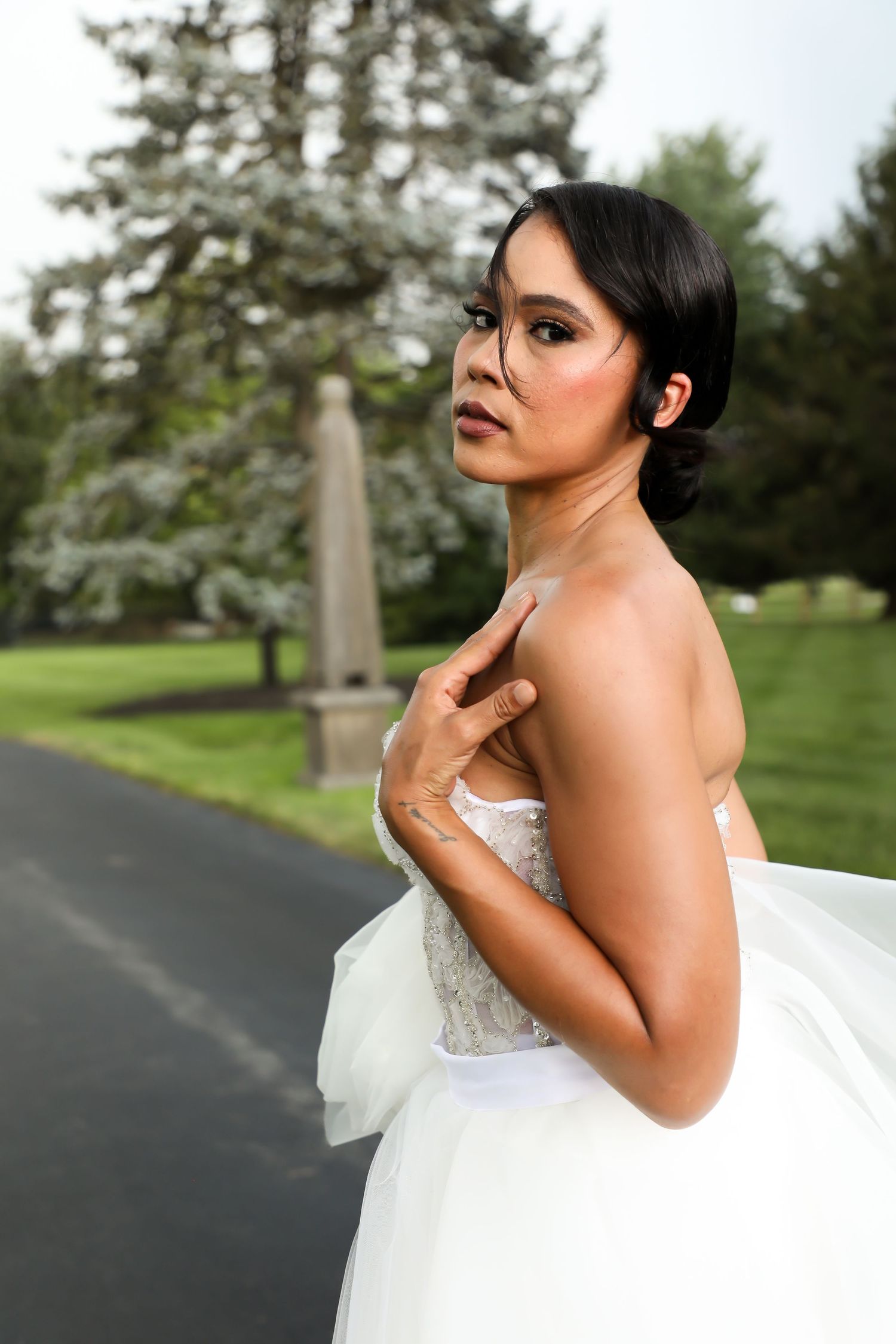 Elegant bride in strapless white gown poses against green outdoor backdrop with dramatic side profile.