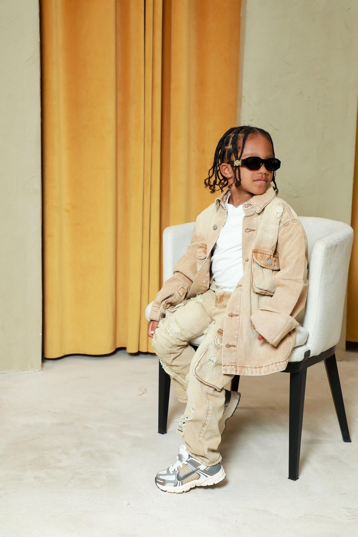 Person in beige outfit and sunglasses sitting casually in white chair.