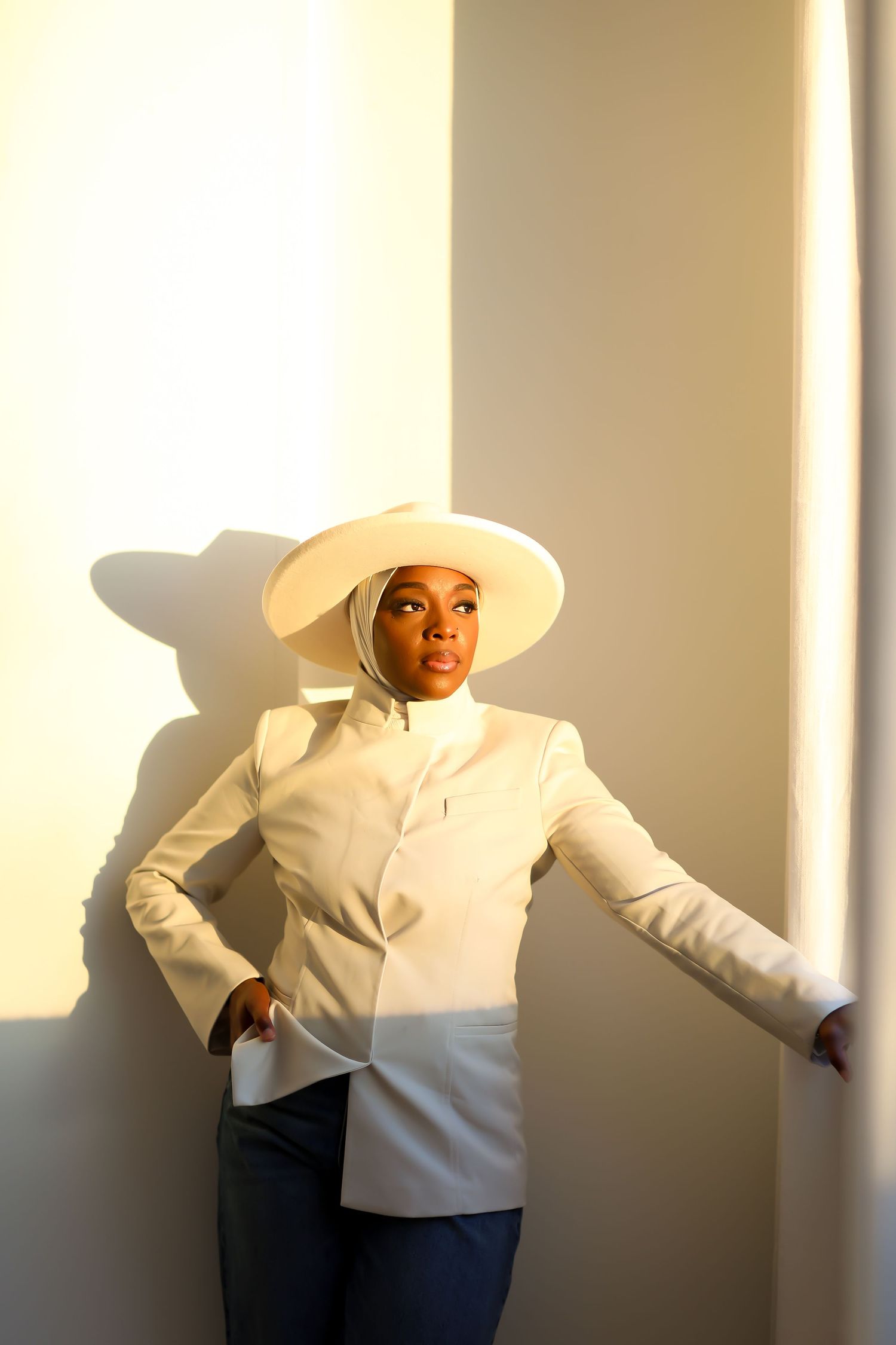 Person in white outfit creating dramatic poses against sunlit wall with strong shadows.