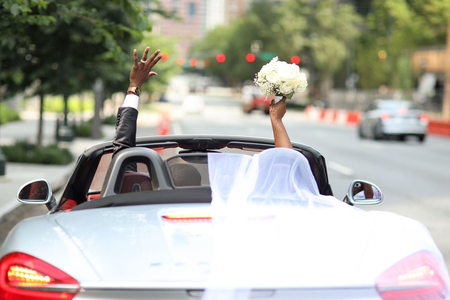 Wedding processional with people waving from decorated cars on a sunny day.
