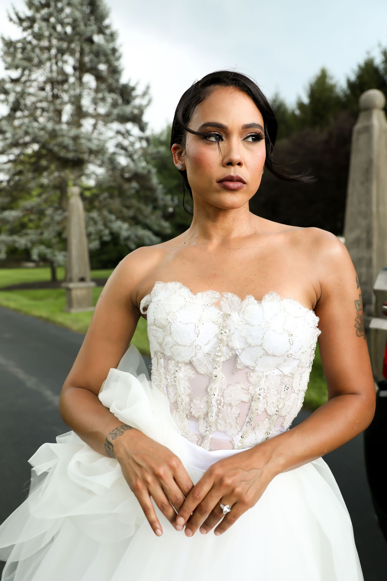 Bride in strapless white ballgown with intricate lace details poses outdoors.