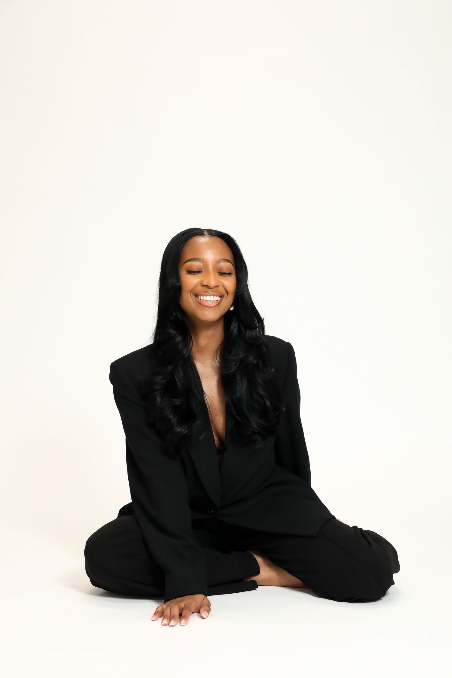 Woman in elegant black outfit lying down and laughing against white background in artistic photo series.