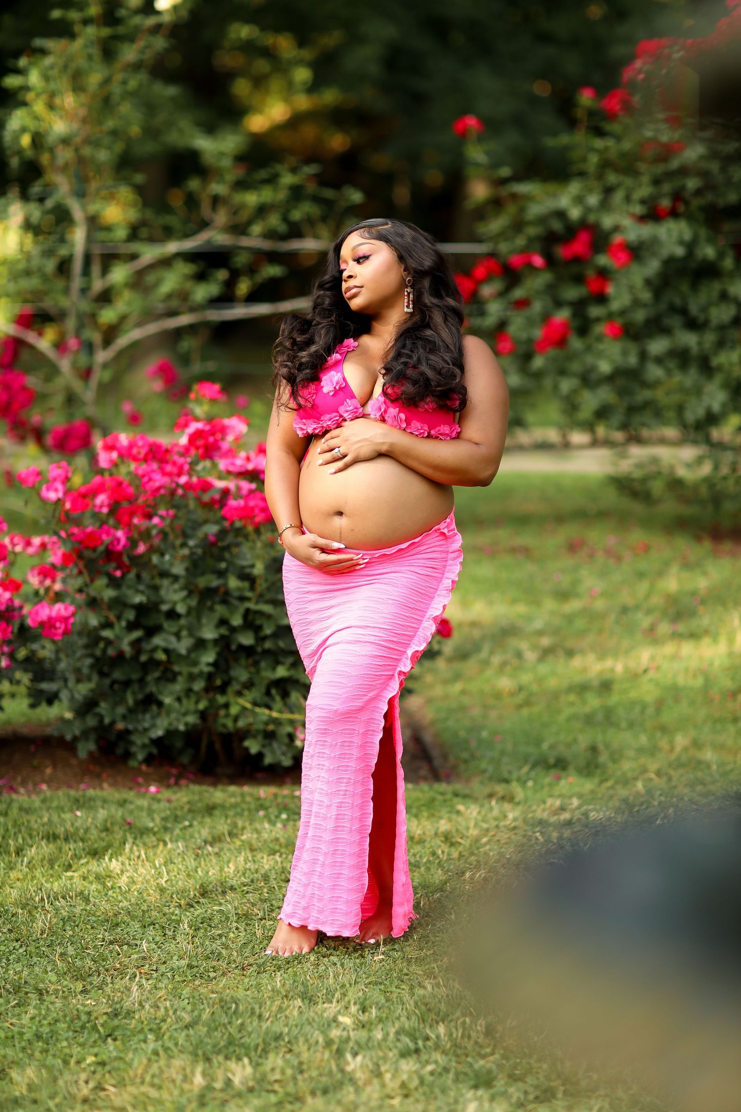 Intimate maternity photos captured in garden with vibrant pink roses.