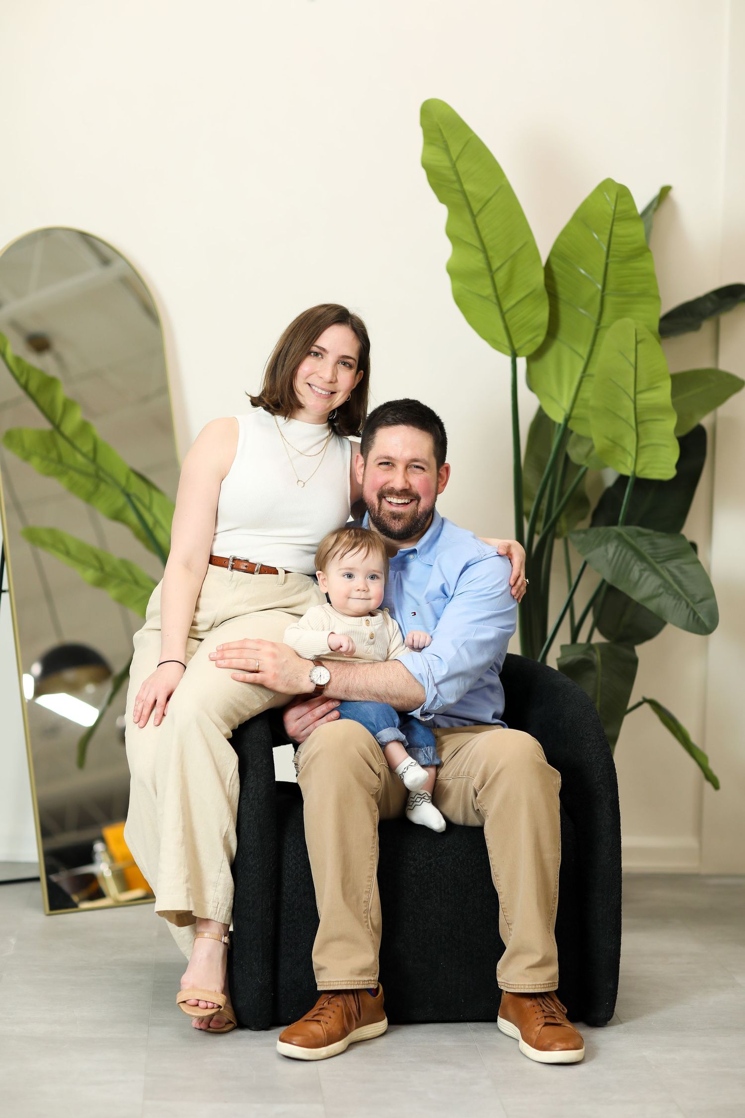 Family sitting together on white bench with large green plants in background.