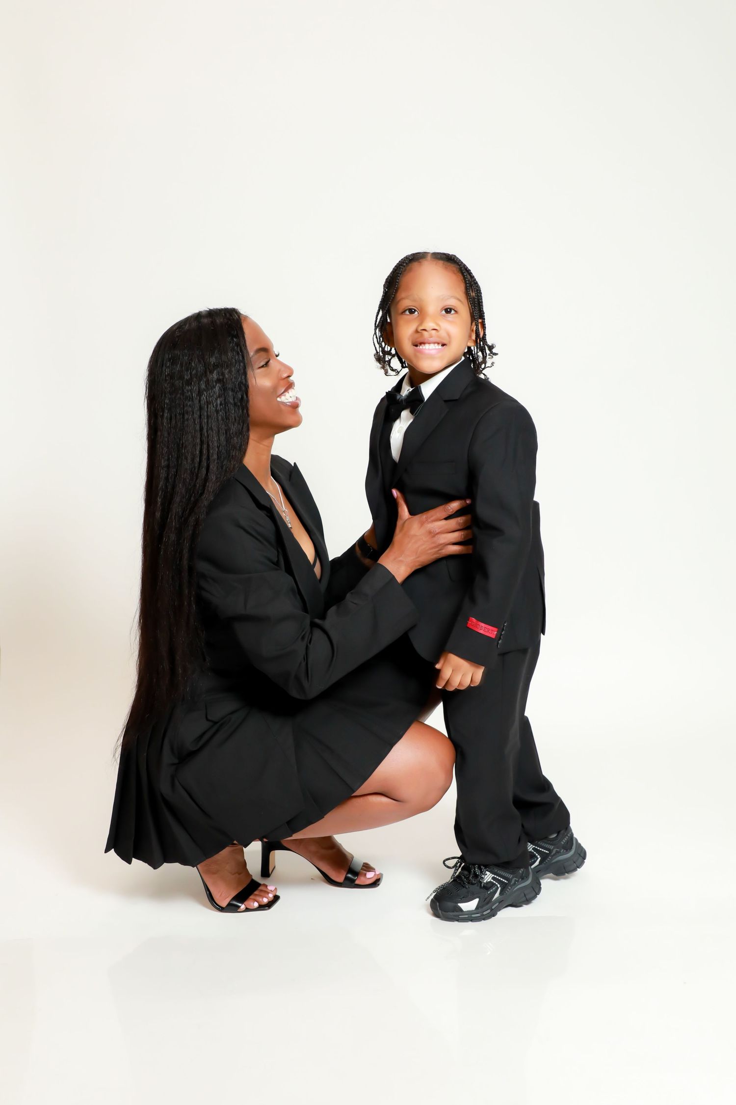 A parent and child wearing matching black outfits share tender moments in a series of studio portraits on white background. Mommy