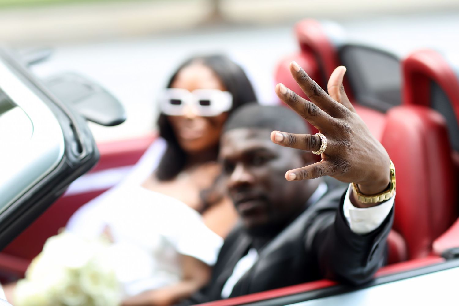 Wedding party rides in a convertible car during a celebration procession.