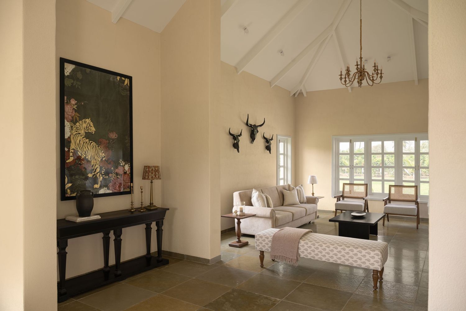 Elegant living room with vaulted ceiling, chandelier, animal skull decor, large leopard artwork, and neutral-toned furniture.