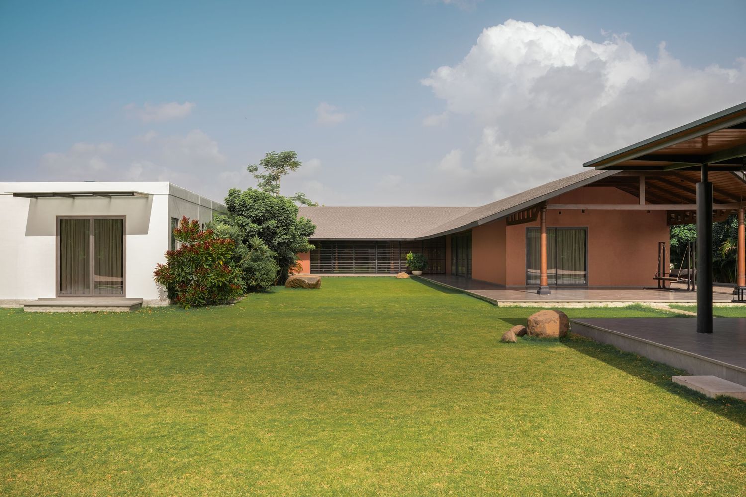 Wide-angle view of terracotta and white modern home with pitched roof, open pavilion, and manicured green lawn under blue sky.