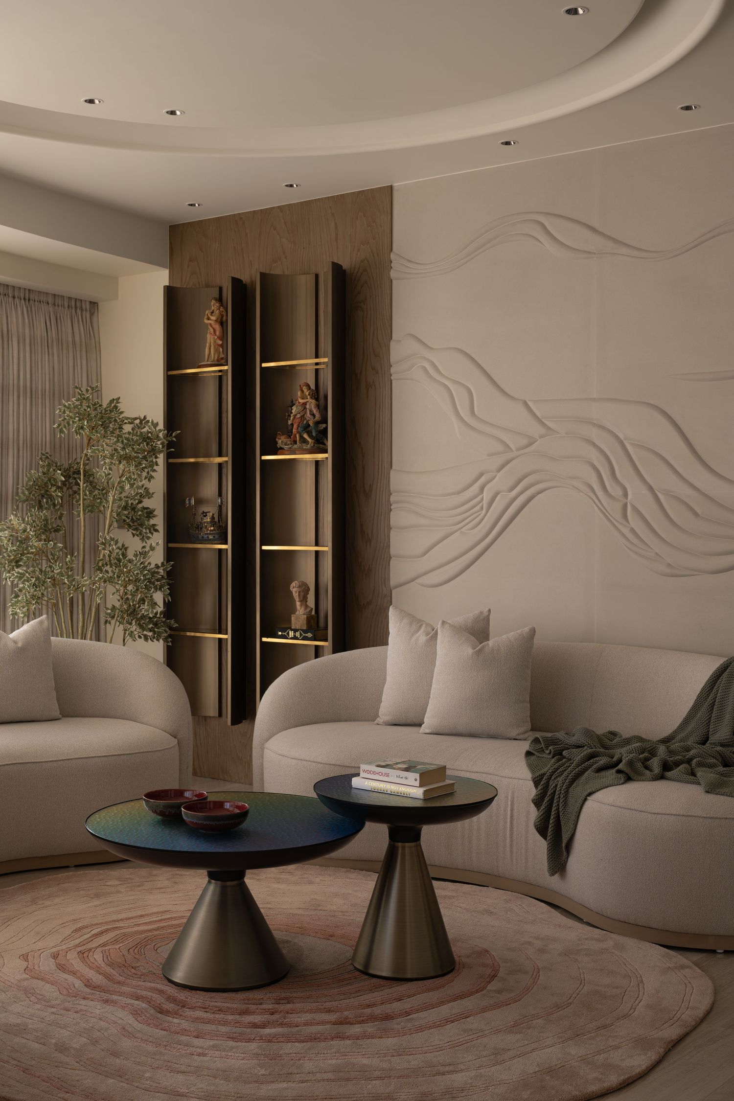 Luxury living room with sculptural white sofas, dark wood shelving unit, abstract wall relief, and round rug.