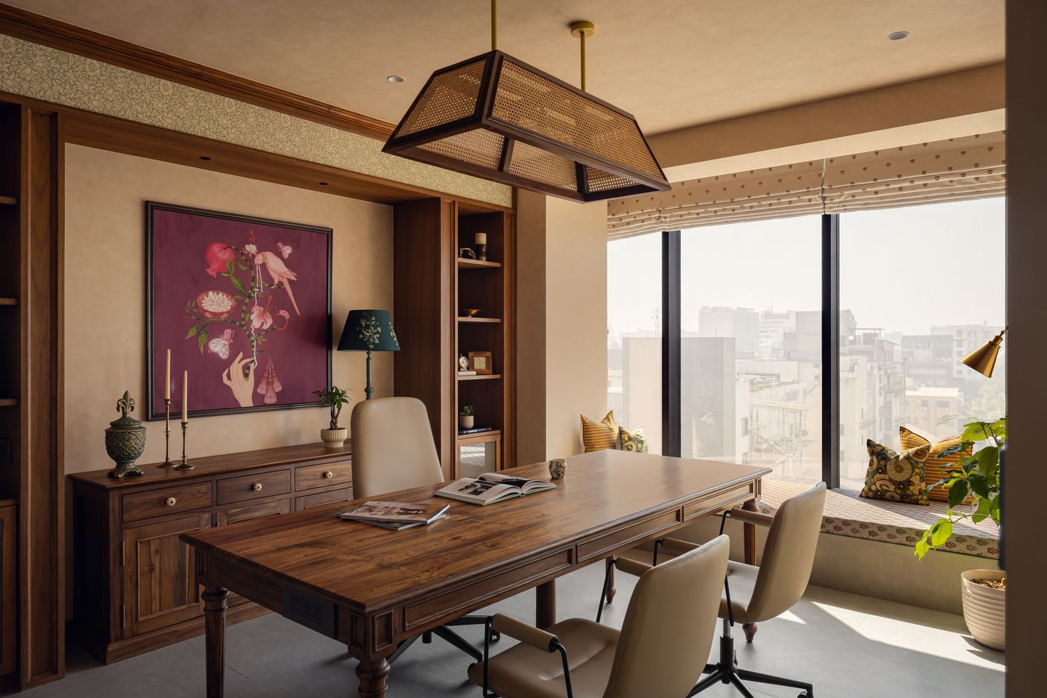 Elegant home office with dark wood desk, neutral chairs, magenta botanical art, pendant light, and panoramic city windows.