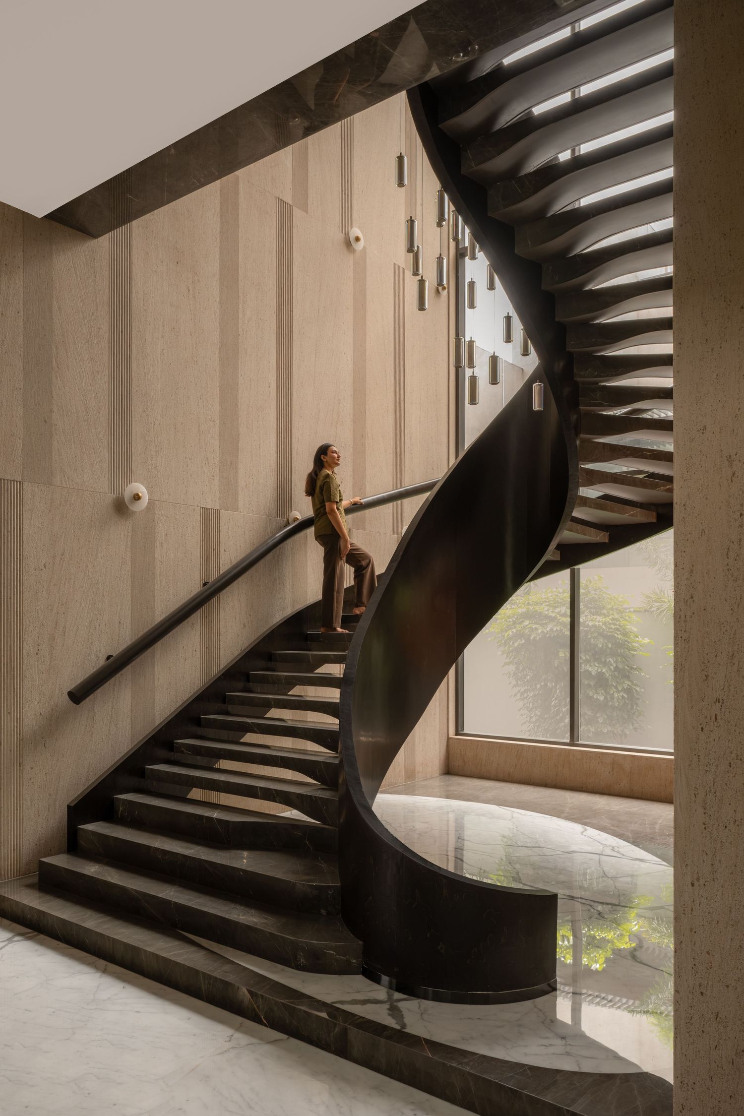 Person ascending a curved spiral staircase with dark metal railings in a modern building with wood-paneled walls.