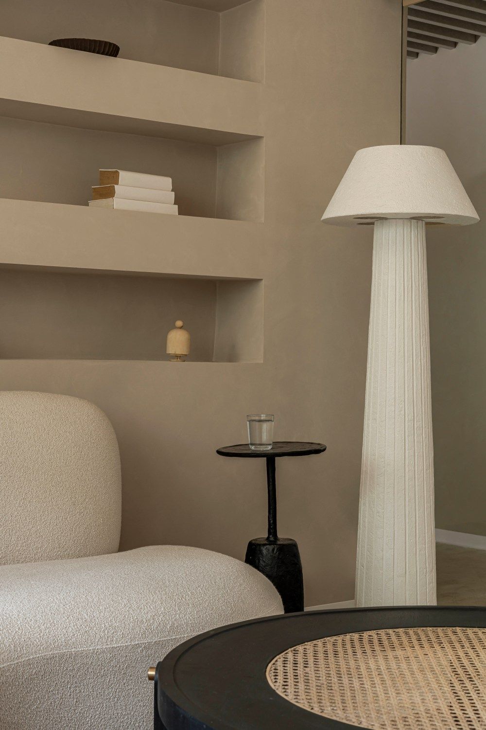 Modern living room featuring white boucle sofa, fluted floor lamp, black side table, and built-in shelves with decor.