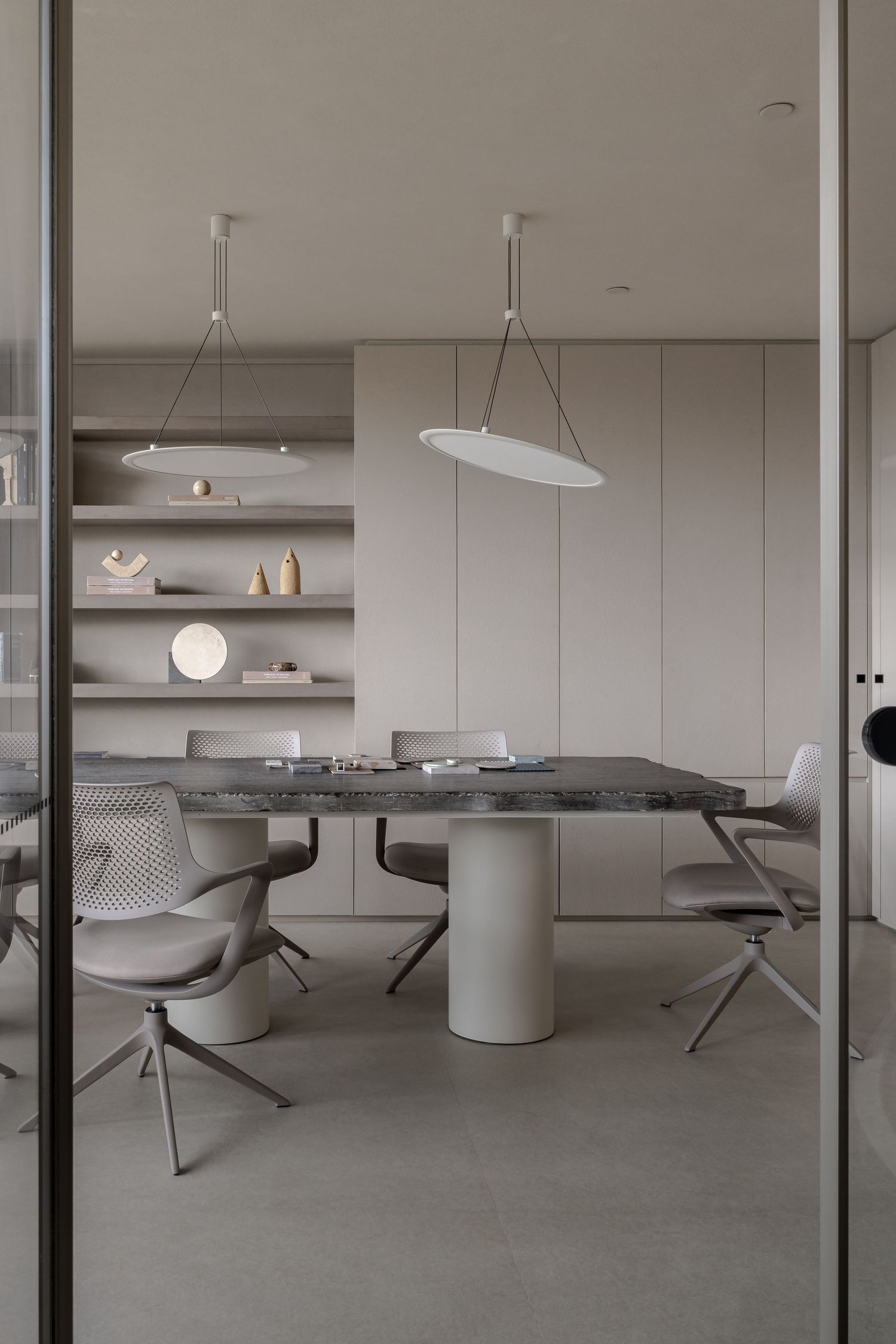 Minimalist dining room with gray marble table, white pendant lights, and neutral-toned chairs on a gray tile floor.