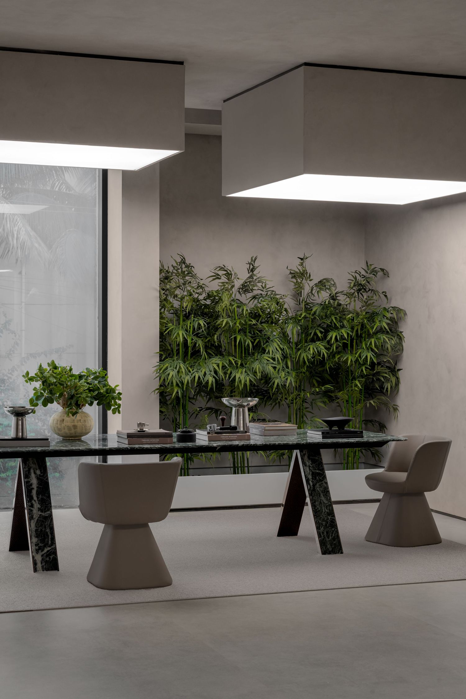Modern dining room with black marble table, taupe chairs, square pendant lights, and bamboo plant wall backdrop.