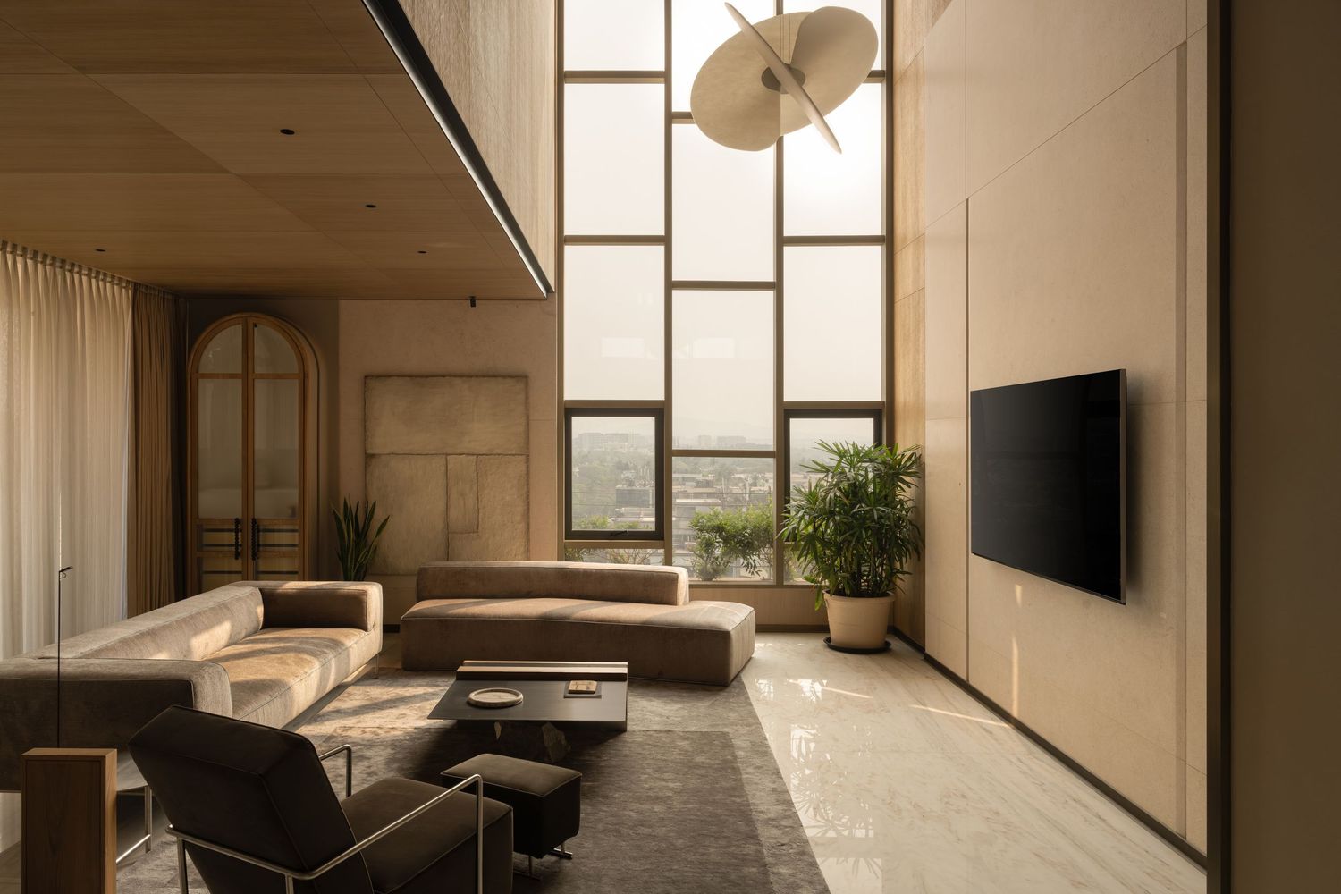 Luxury double-height living room with floor-to-ceiling windows, brown sectional sofa, statement pendant light, and wall-mounted TV.