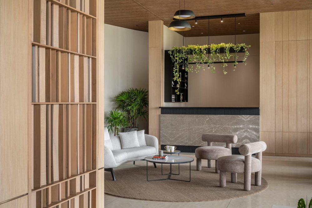 Contemporary lobby lounge with hanging plants, marble accent wall, white sofa, round ottomans, and wood panel walls.