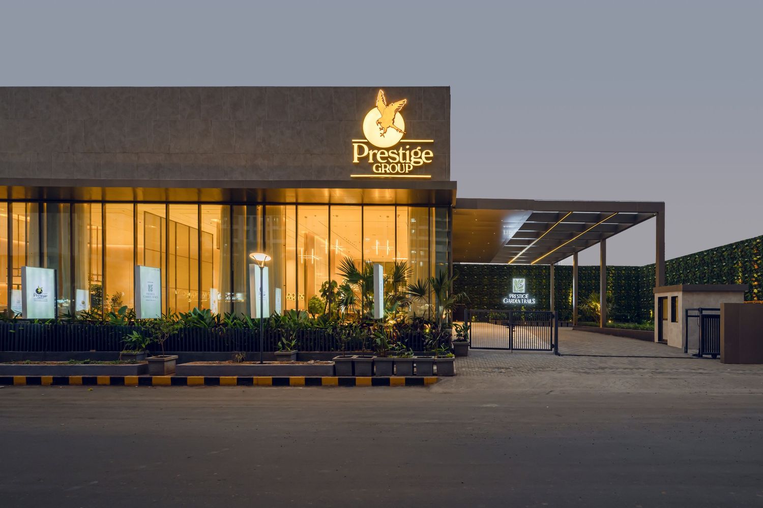 Prestige Group branded building exterior illuminated at dusk with golden signage and manicured landscaping.
