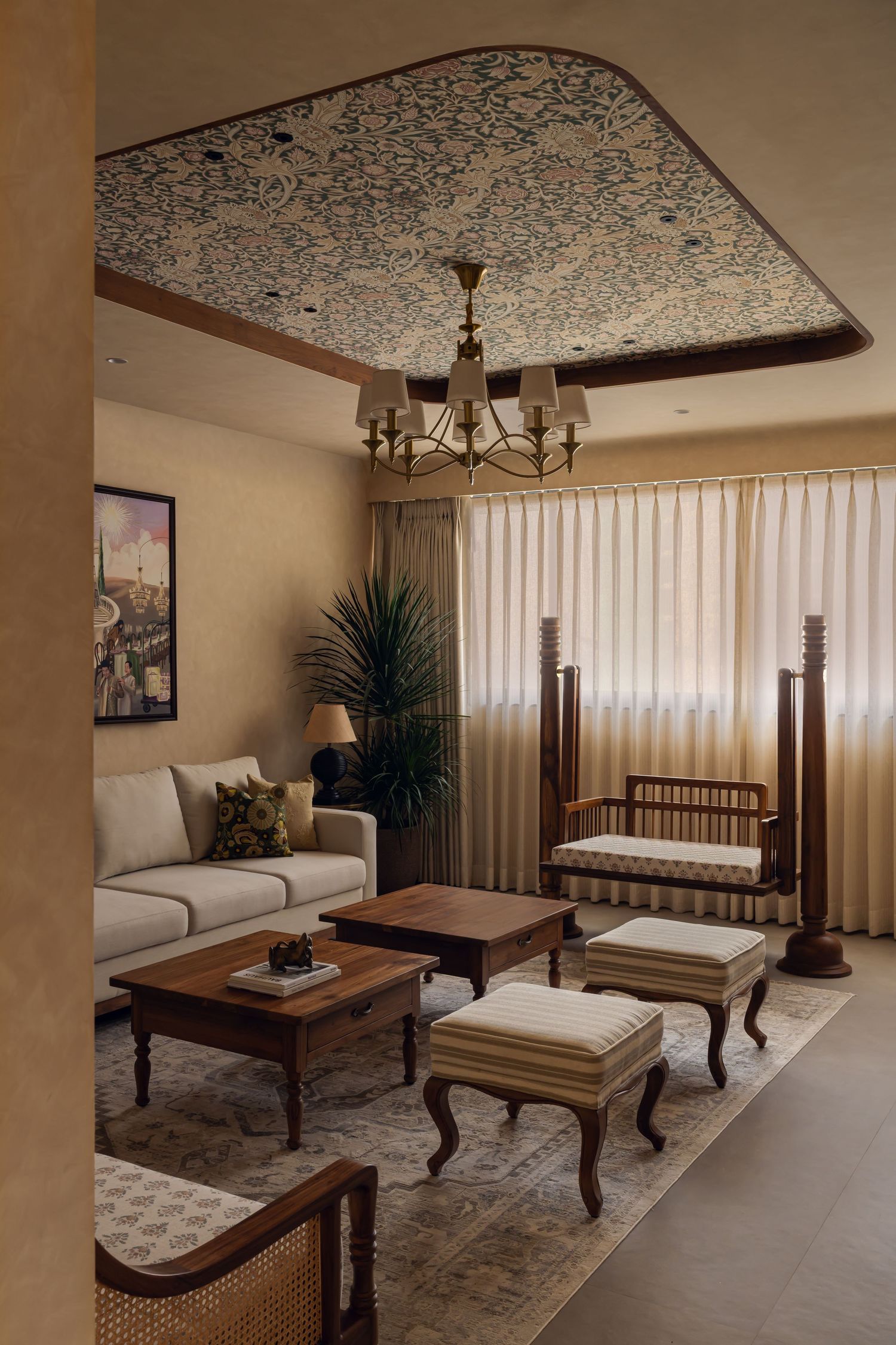 Traditional living room with ornate blue patterned ceiling, brass chandelier, wooden furniture, and sheer curtain windows.