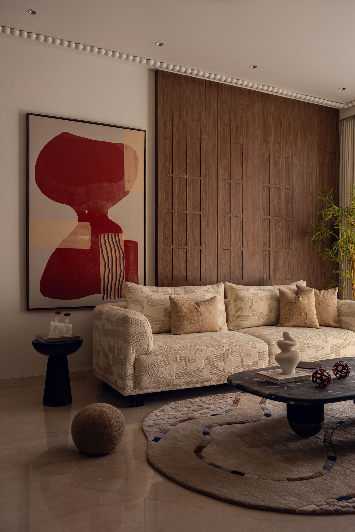Modern living room with cream textured sofa, bold red abstract artwork, dark coffee table, and wood panel wall.