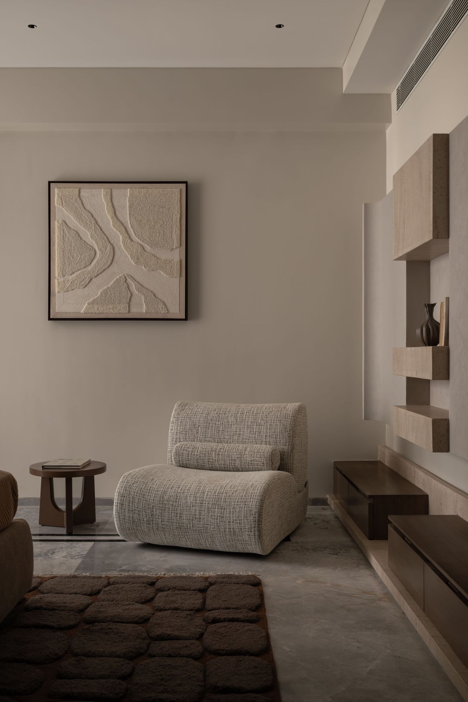 Minimalist room with bouclé lounge chair, textured wall art, dark wood side table, and built-in shelving.